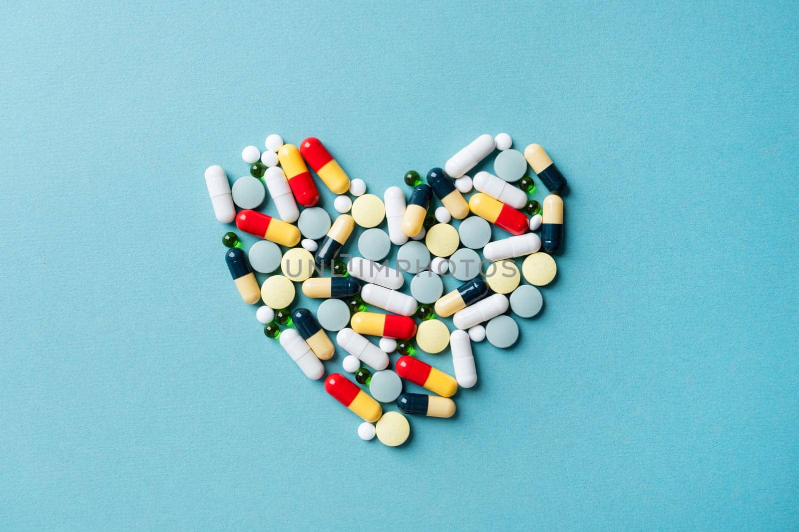 Pills forming heart shape on blue background, copy space