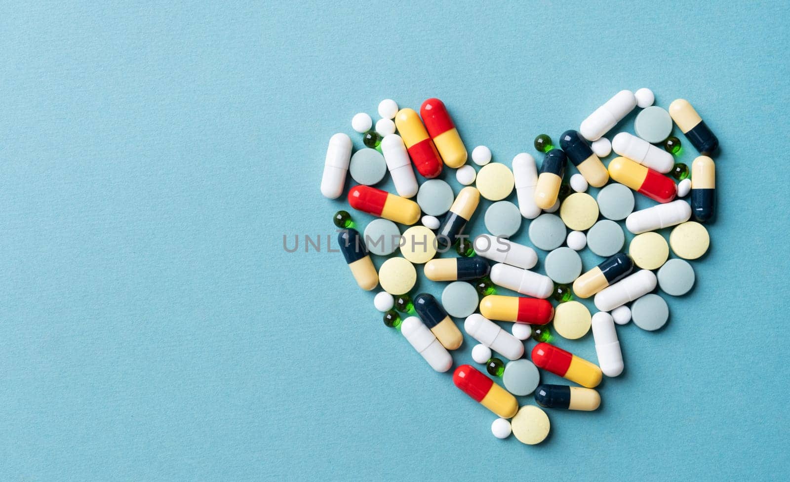 Pills forming heart shape on blue background, copy space