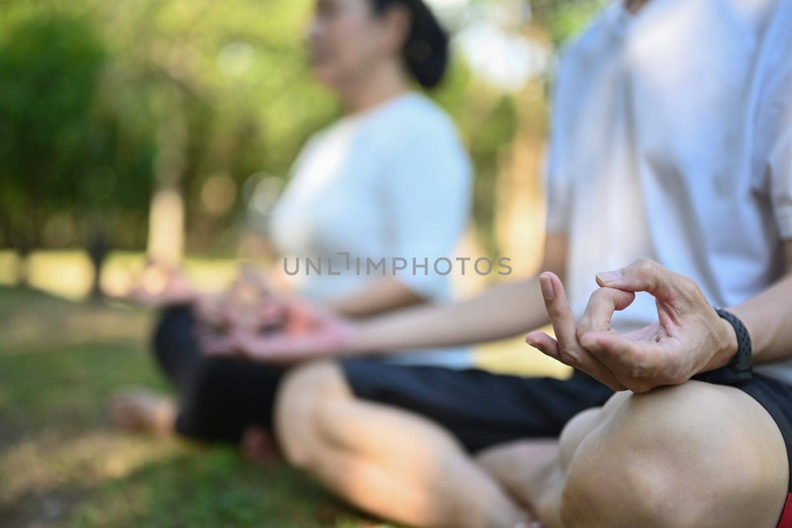 Close up shot of senior couple meditating sitting in lotus pose at summer park. Healthy lifestyle concept