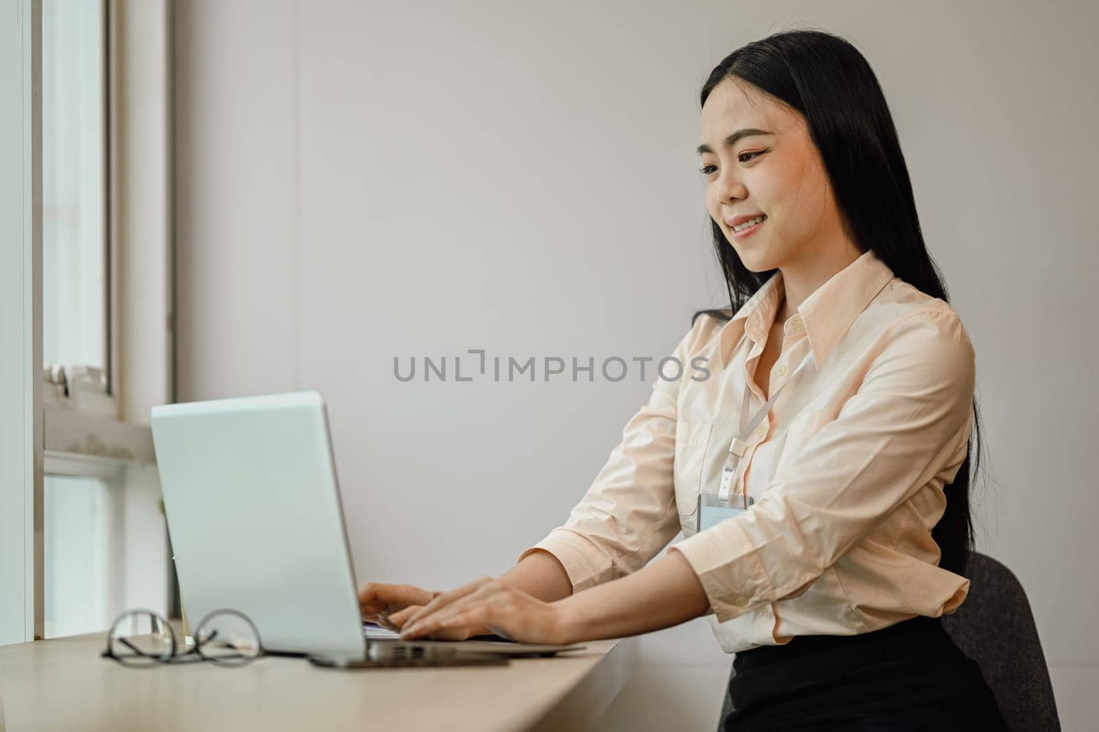 Attractive Asian female employee typing on laptop while working over presentation in bright office