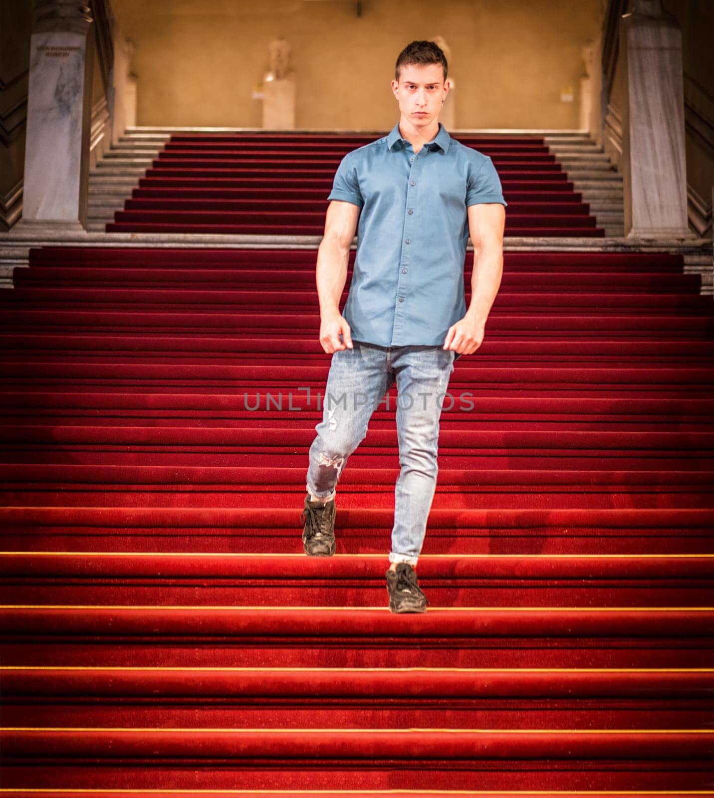 A young fit man standing on a red carpeted staircase, walking down.