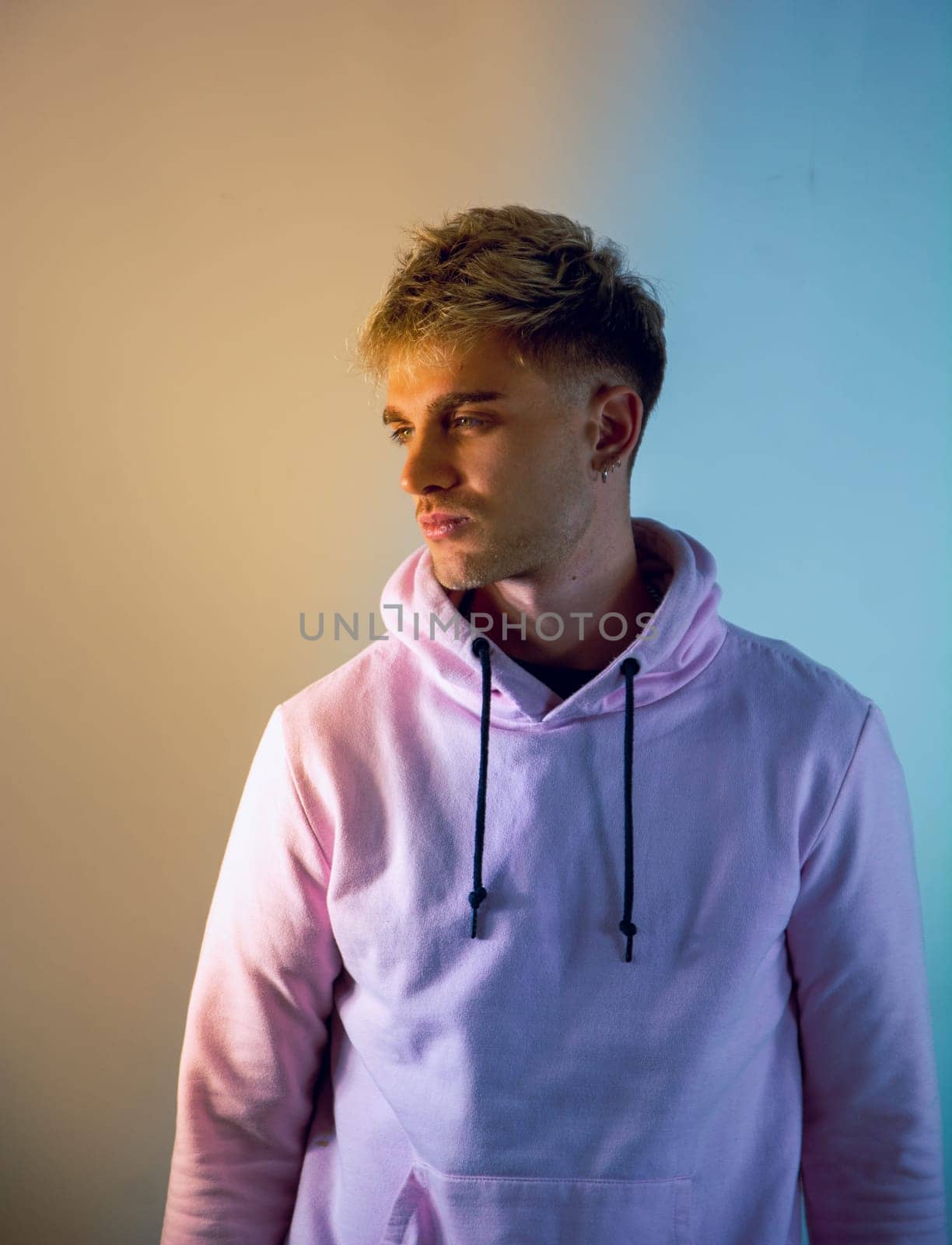 Attractive blond young man with blue eyes, wearing pink sweater, in studio shot on neutral background