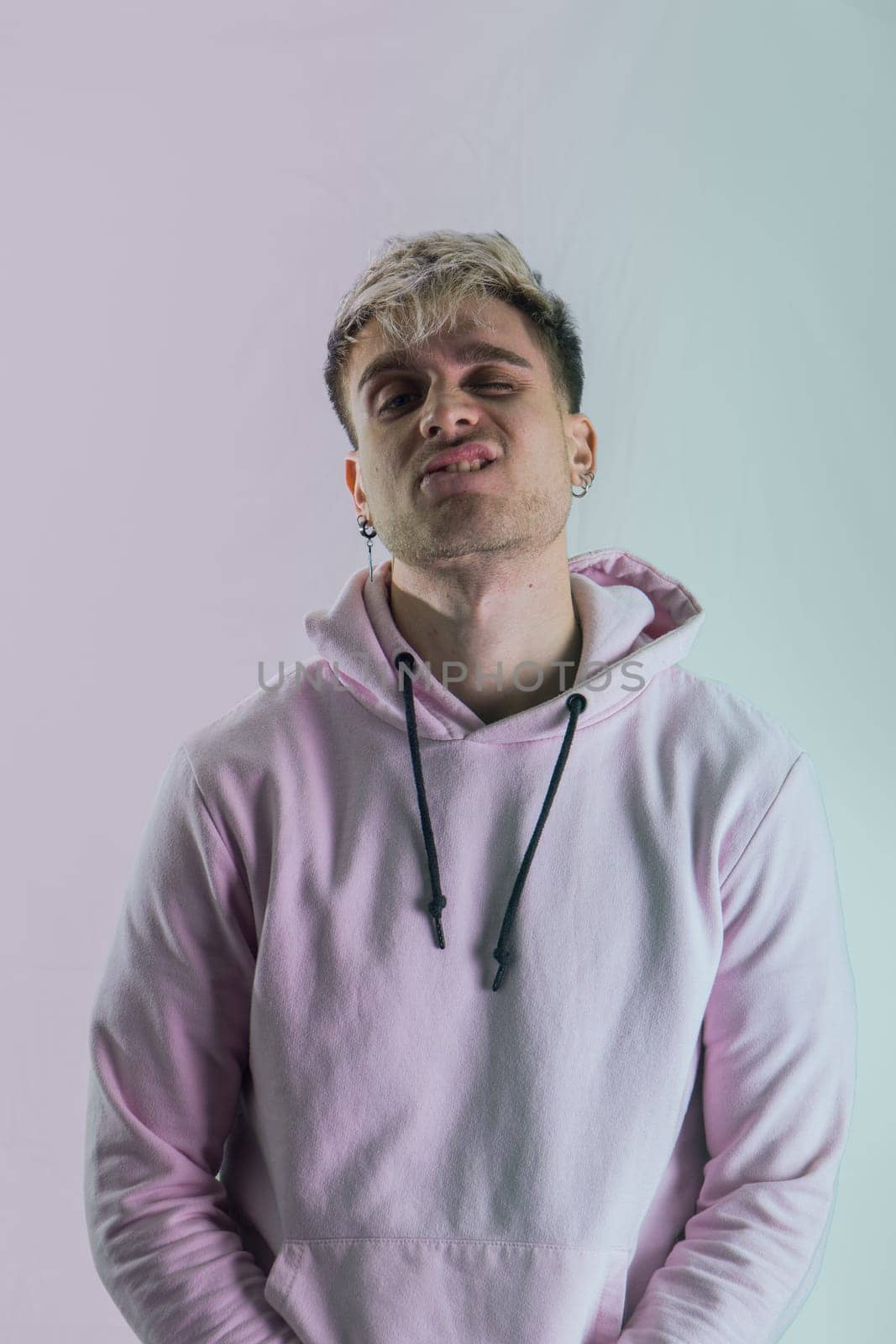 Attractive blond young man with blue eyes, wearing pink sweater, in studio shot on neutral background