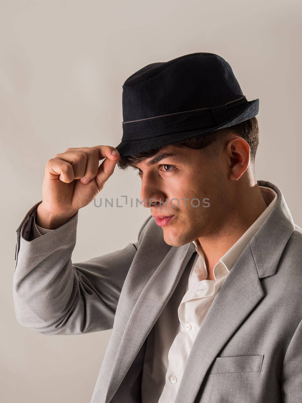 Attractive elegant young man with business suit and fedora hat, on white, looking away, seen sideways