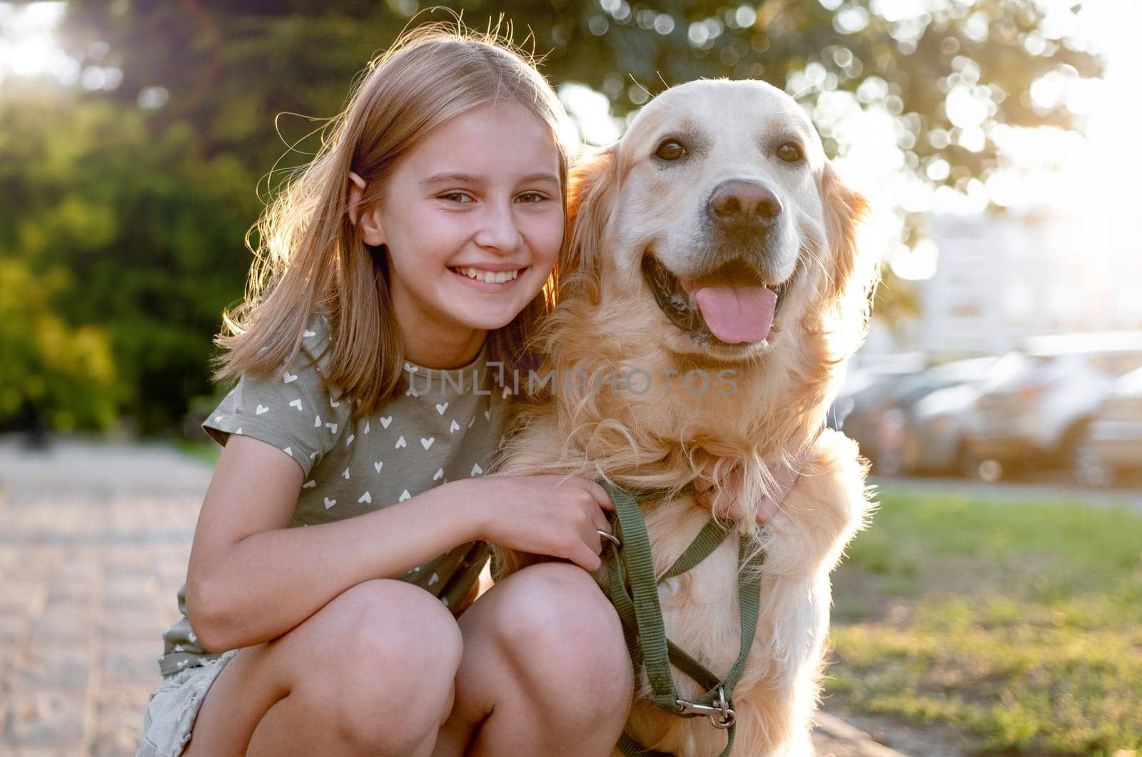 Cute preteen child girl hugging golden retriever dog at nature. Pretty kid petting purebred doggy pet labrador at park and smiling