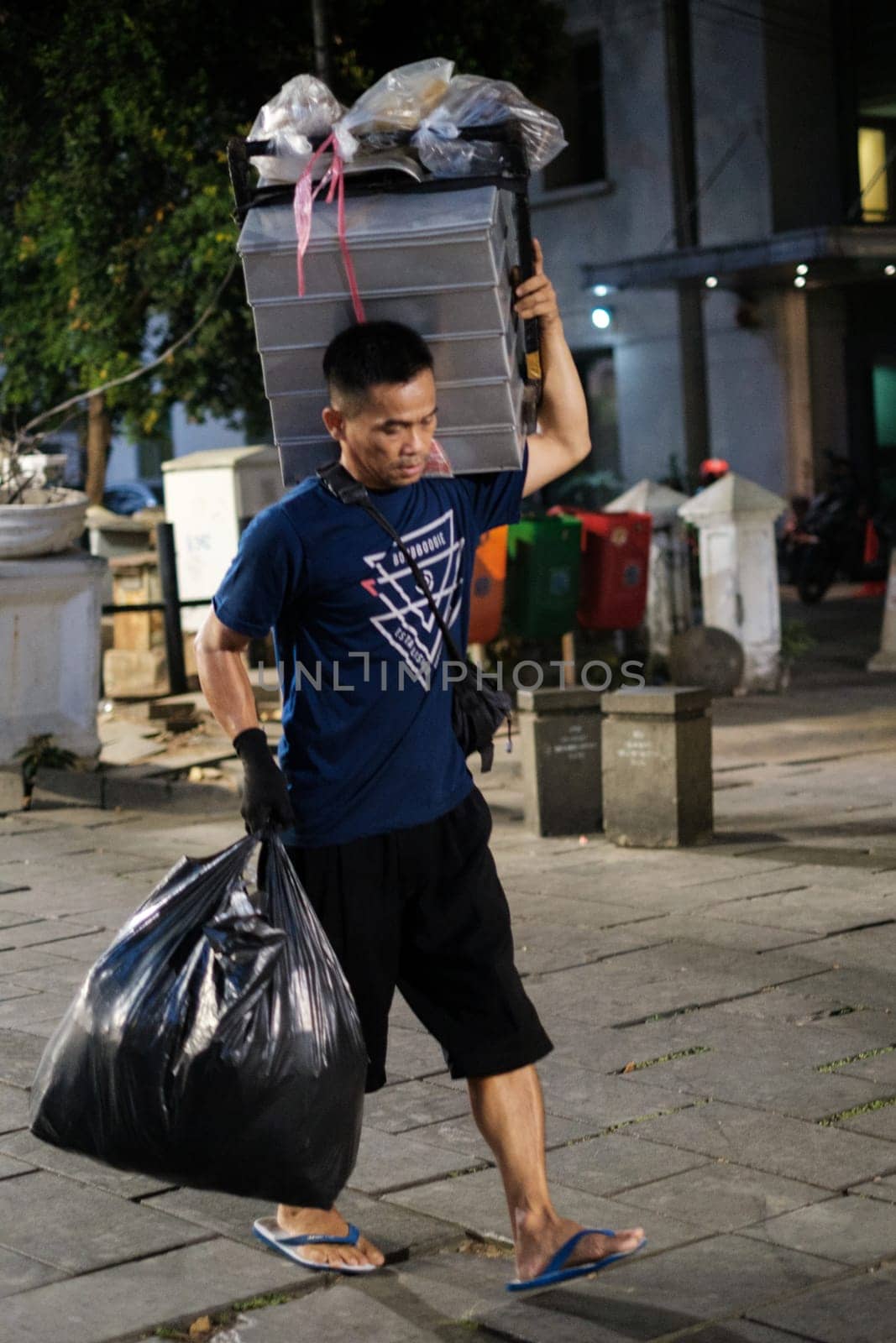 Jakarta, Indonesia - October 2 2023: Man Carrying Heavy Loads Across Street by jinhongljh
