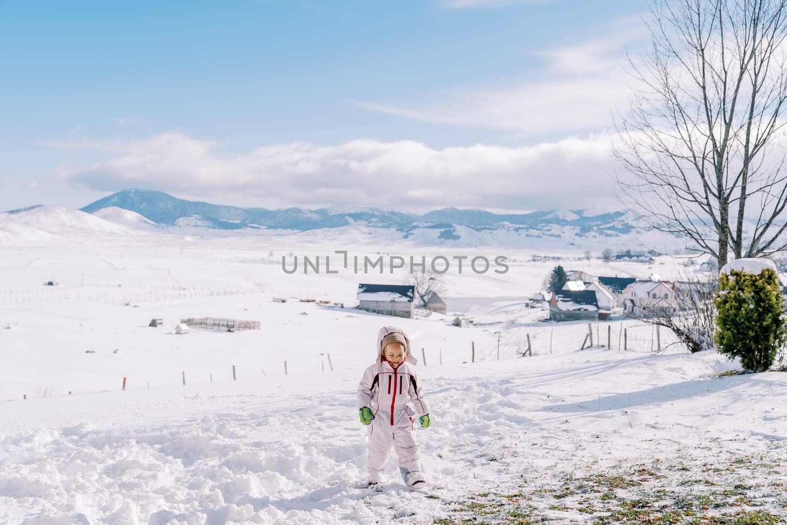 Little girl walks on a snowy plain in the mountains, looking at her feet. High quality photo