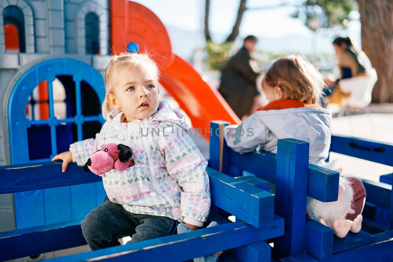 Little girl sits on a bench in the playground and looks away. High quality photo
