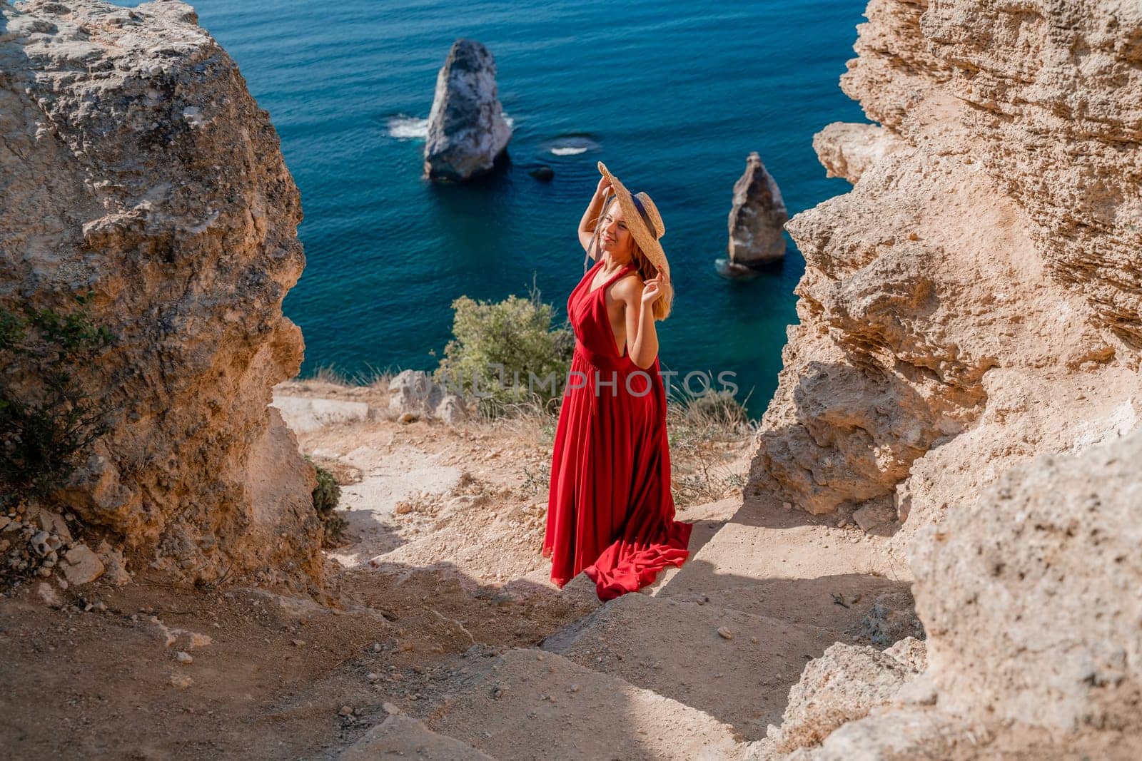 A woman in a flying red dress fluttering in the wind and a straw hat against the backdrop of the sea