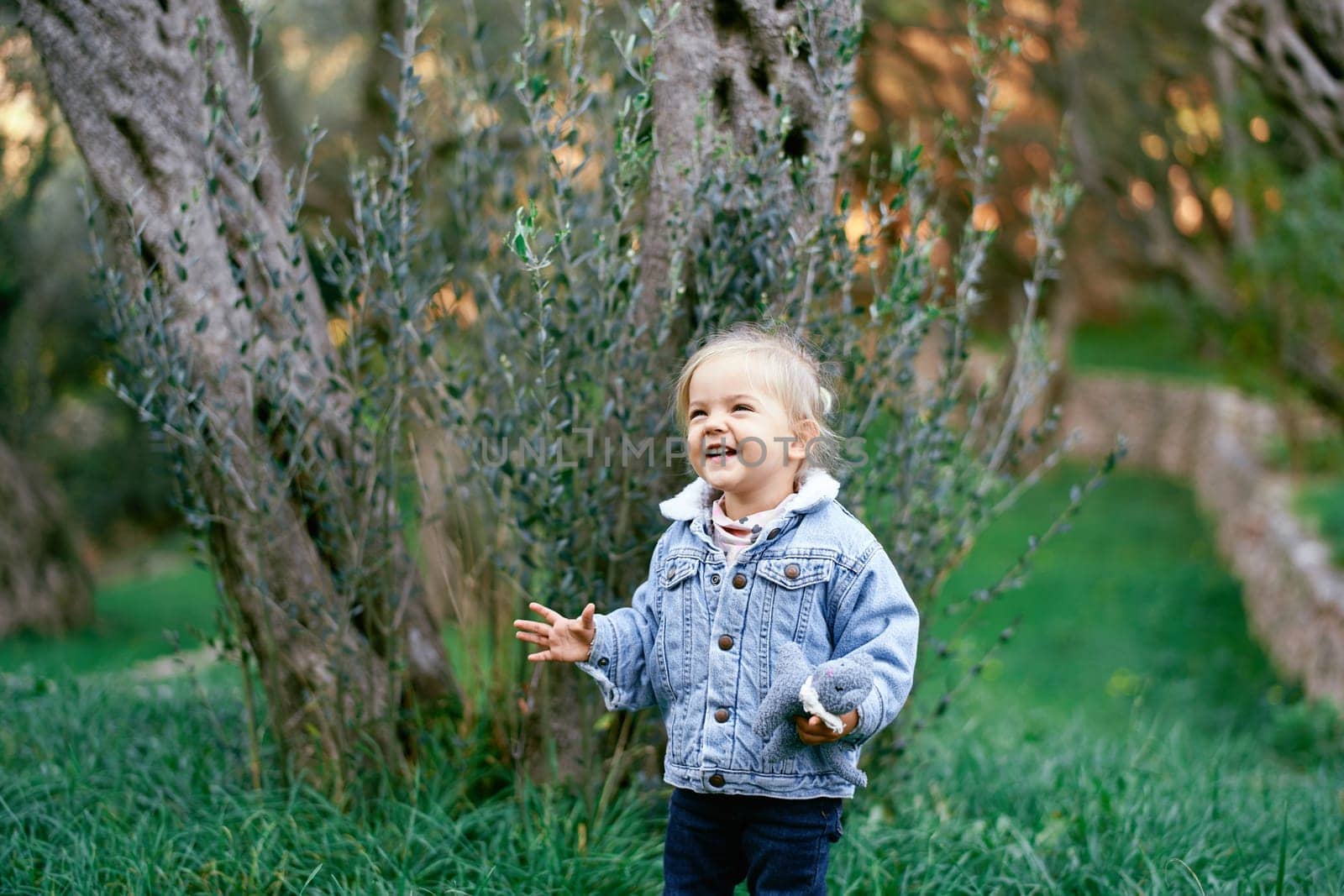Little laughing girl stands near the tree with a soft toy in her hand. High quality photo