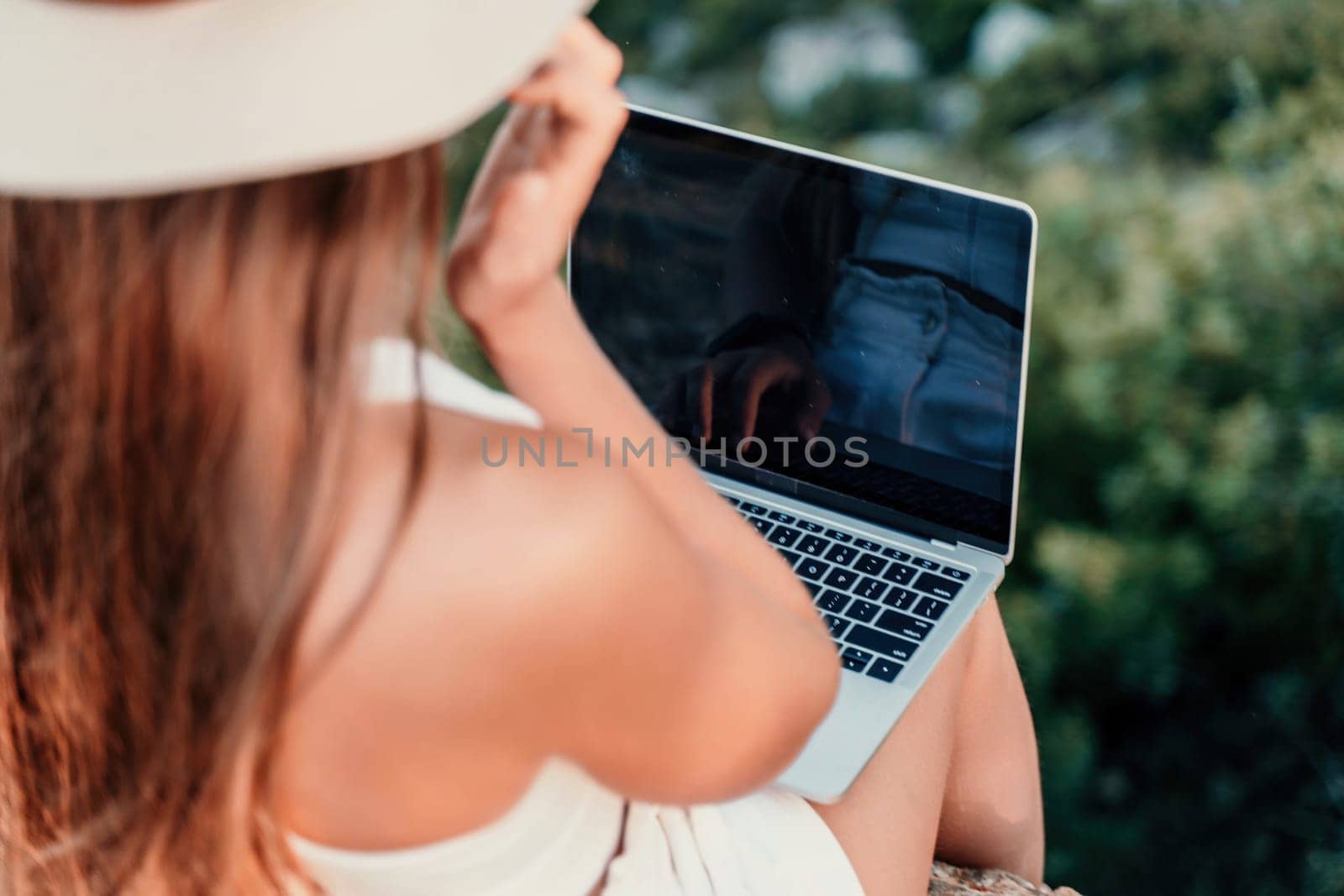 Freelance women sea working on the computer. Good looking middle aged woman typing on a laptop keyboard outdoors with a beautiful sea view. The concept of remote work