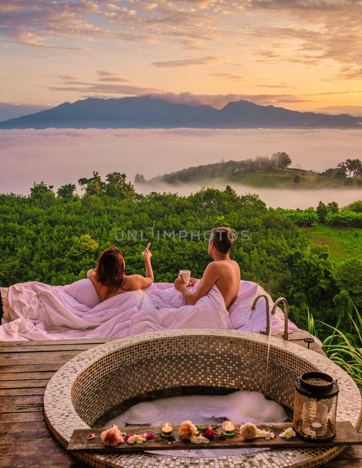 a couple of men and women in an outdoor bed looking out over the mountains of Northern Thailand during vacation. Outdoor bathroom, and bathtub during sunset at the mountains with mist and fog