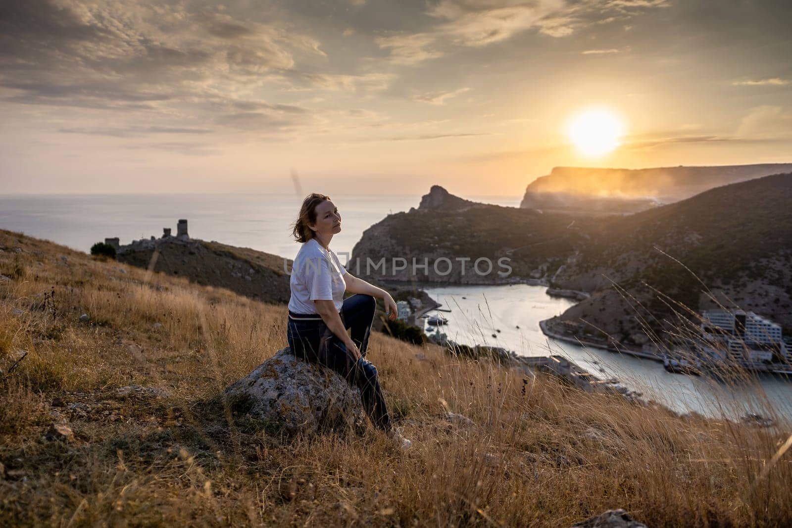 Happy woman on sunset in mountains. Woman siting with her back on the sunset in nature in summer. Silhouette. by Matiunina