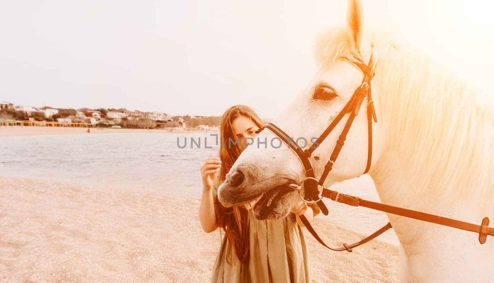 A white horse and a woman in a dress stand on a beach, with the sky and sea creating a picturesque backdrop for the scene