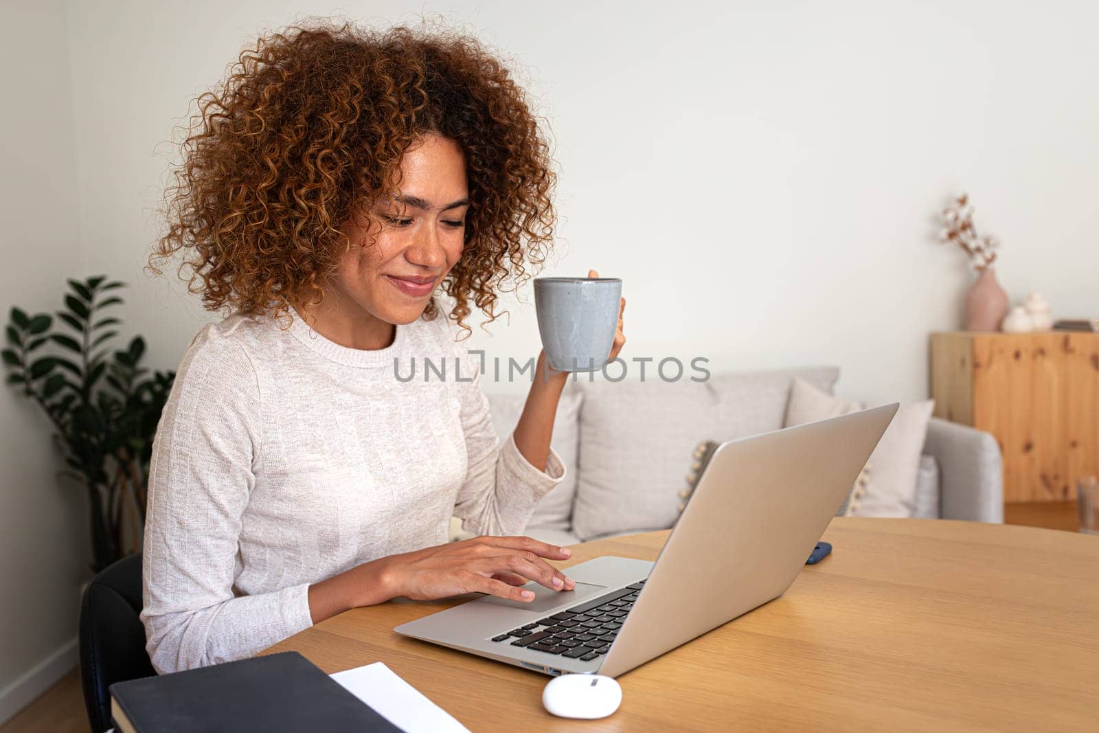 Multiracial woman working at home office having coffee. African American female entrepreneur using laptop. Copy space. by Hoverstock