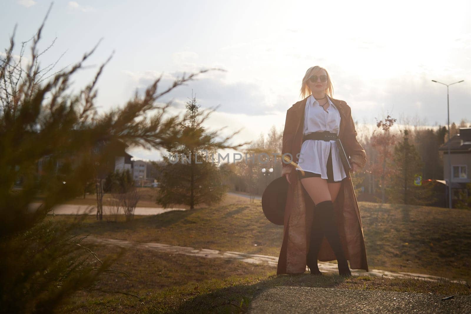 stylish, fashionable, imposing blonde girl in black glasses, a white shirt, a short skirt and a long raincoat with a laptop and hat on the street of the town. Defiantly dressed confident businesswoman by keleny