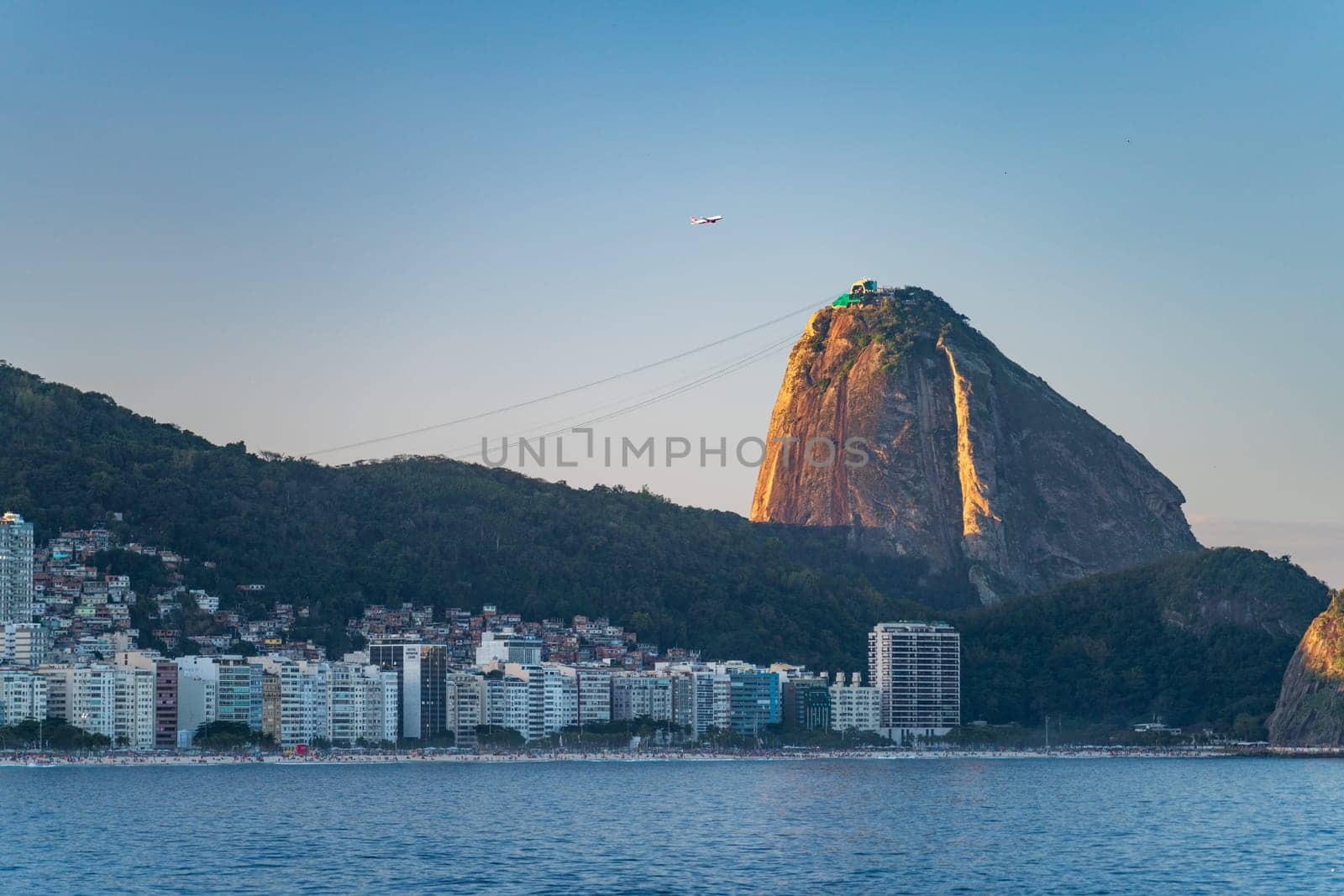 Plane taking off over Rio with Sugarloaf Mountain and Copacabana Beach in view against a blue sky.