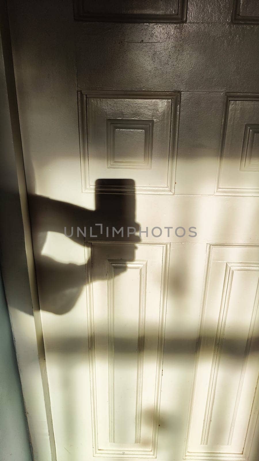 A wooden painted door and shadow from the hands of a man filming on a cell phone. Private detective, crime, mysterious entrance, maniac
