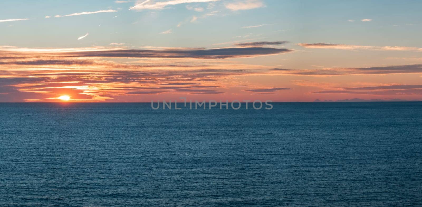 "Tranquil ocean sunset with island silhouettes against a colorful sky."