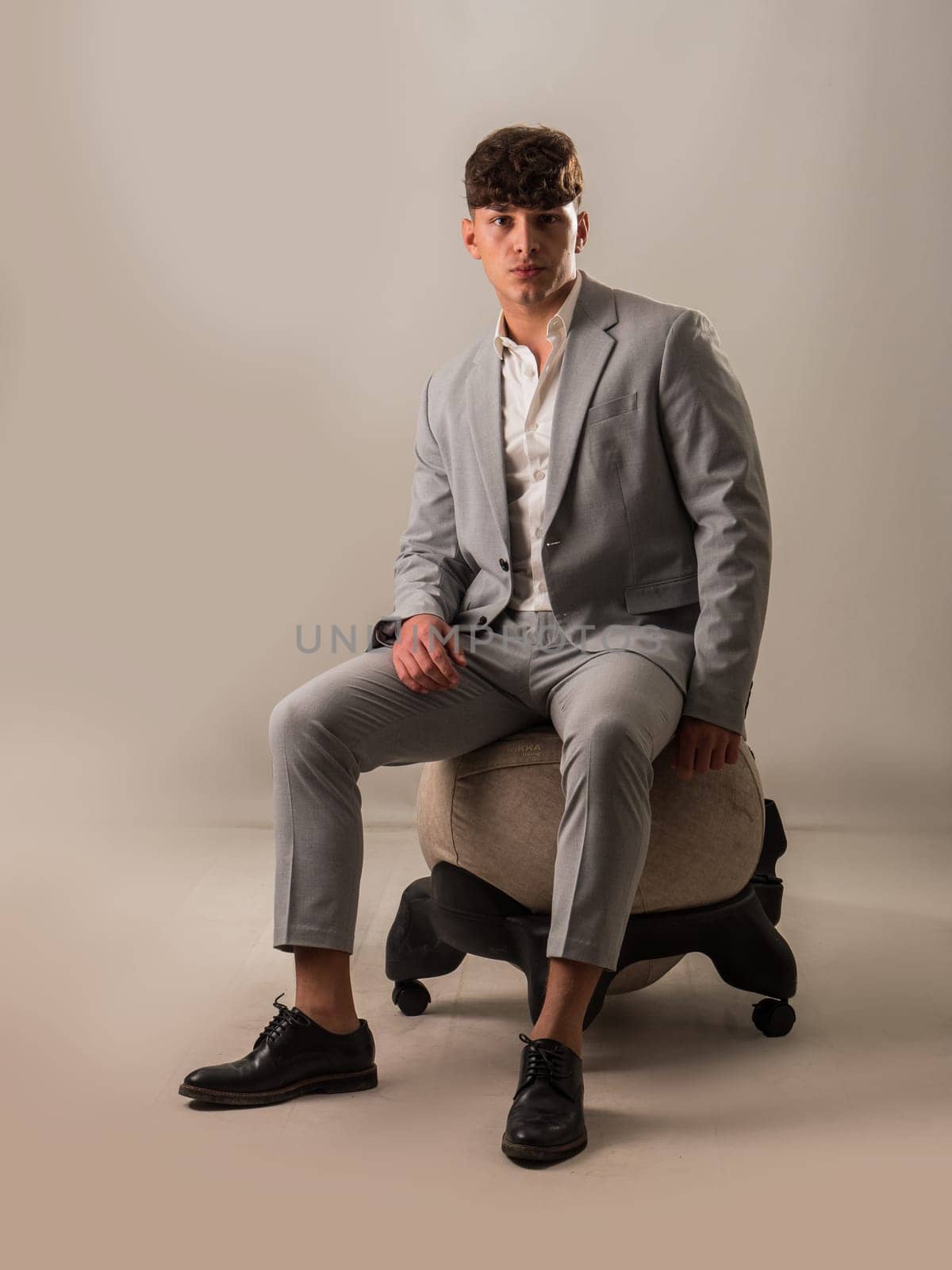 Full figure shot of young handsome man sitting on balance ball chair against white background, elegant young man with business suit