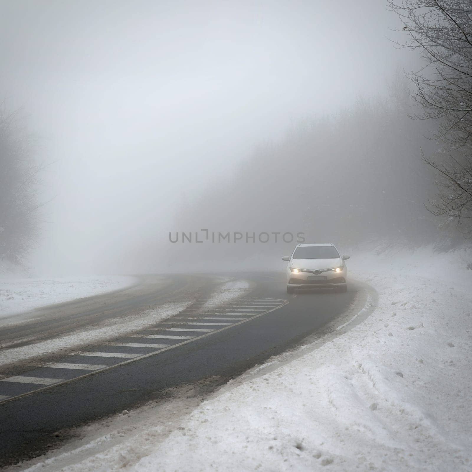 Cars in the fog. Bad winter weather and dangerous automobile traffic on the road. Light vehicles in foggy day. by Montypeter