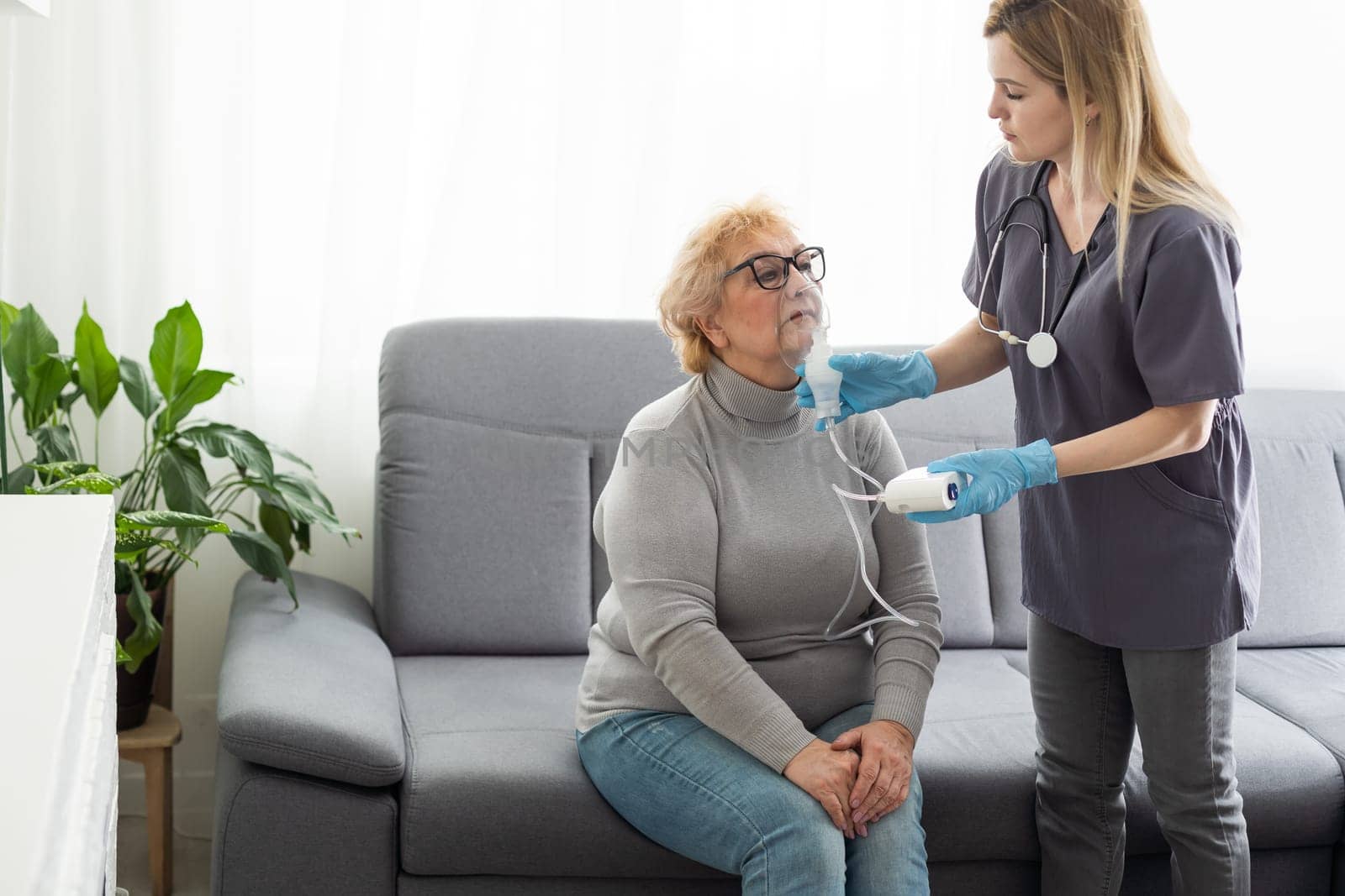 Young girl doctor makes inhalation to an older woman on a white background. Fight nasal congestion and rhinitis