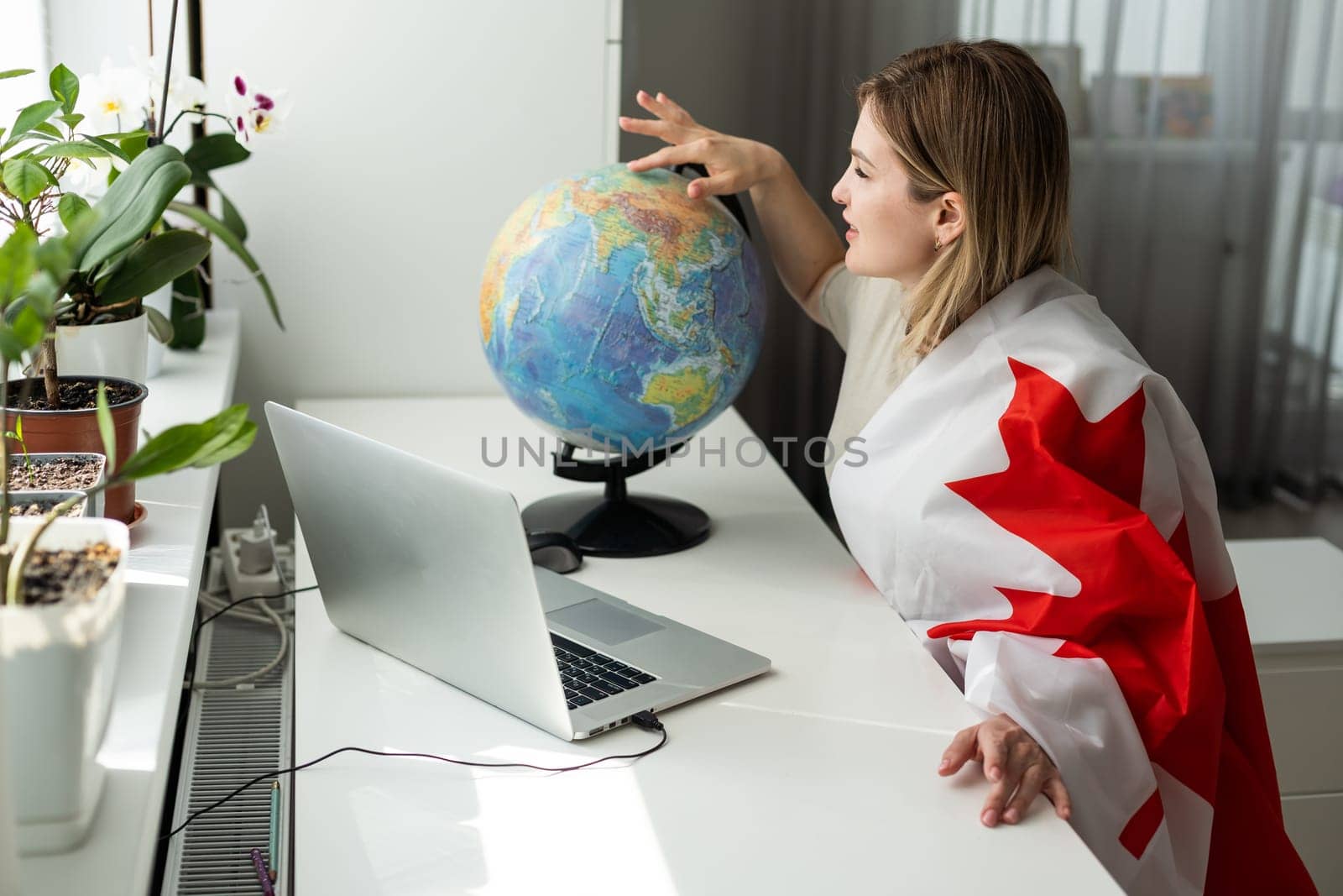 A female hand holds a small canada flag and a laptop on the background of the university. Close up. High quality photo