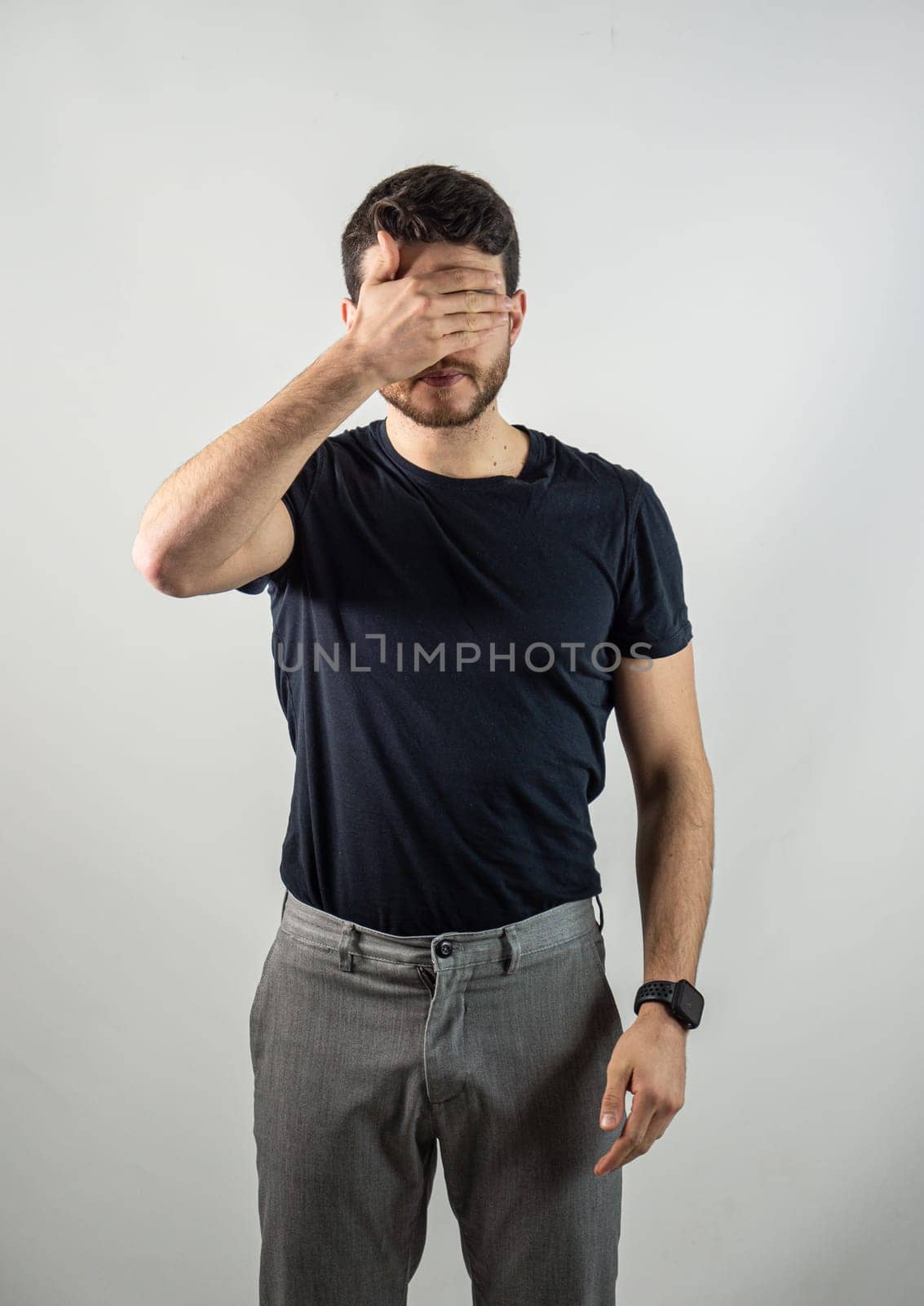 Attractive young man covering eyes with his hands in studio shot. Secret concept.