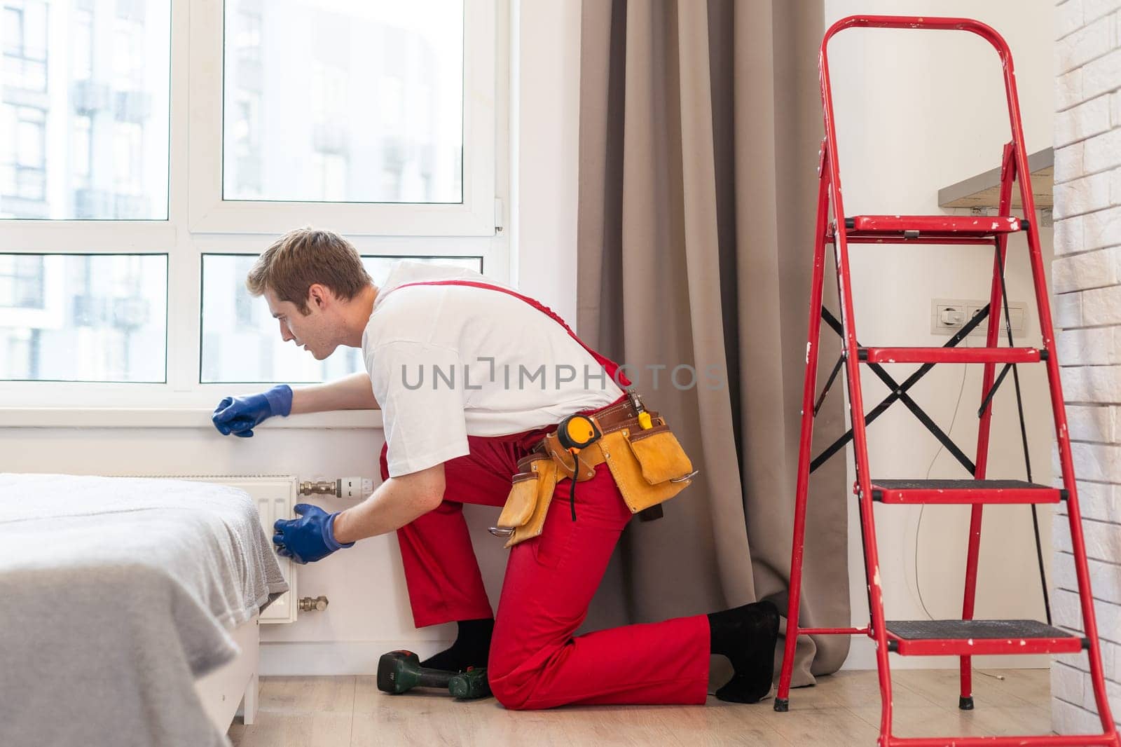 A plumber is fixing a radiator. With an adjustable wrench, he tightens the tap. A briefcase with a tool at hand.