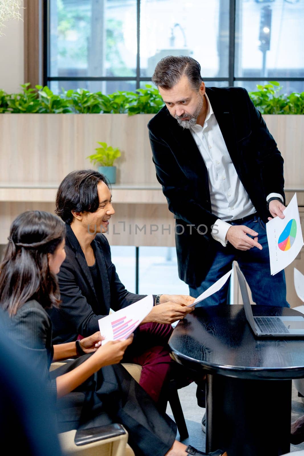 Vertical image of Caucasian manager man stand and hold paper with graph to explain to his colleagues to make the understand of the project. by nrradmin