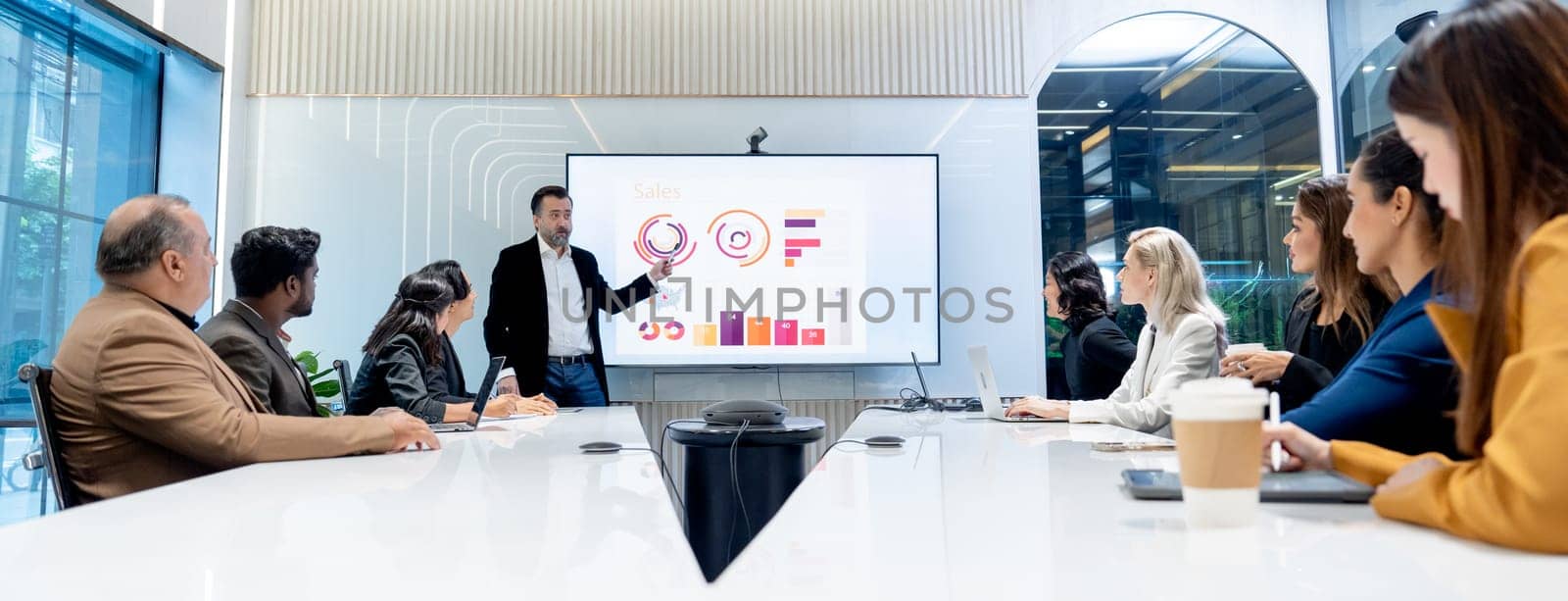 Wide shot of Caucasian man as manager stand in front of conference room to present the business performance using monitor to show information of the company with the staffs. by nrradmin