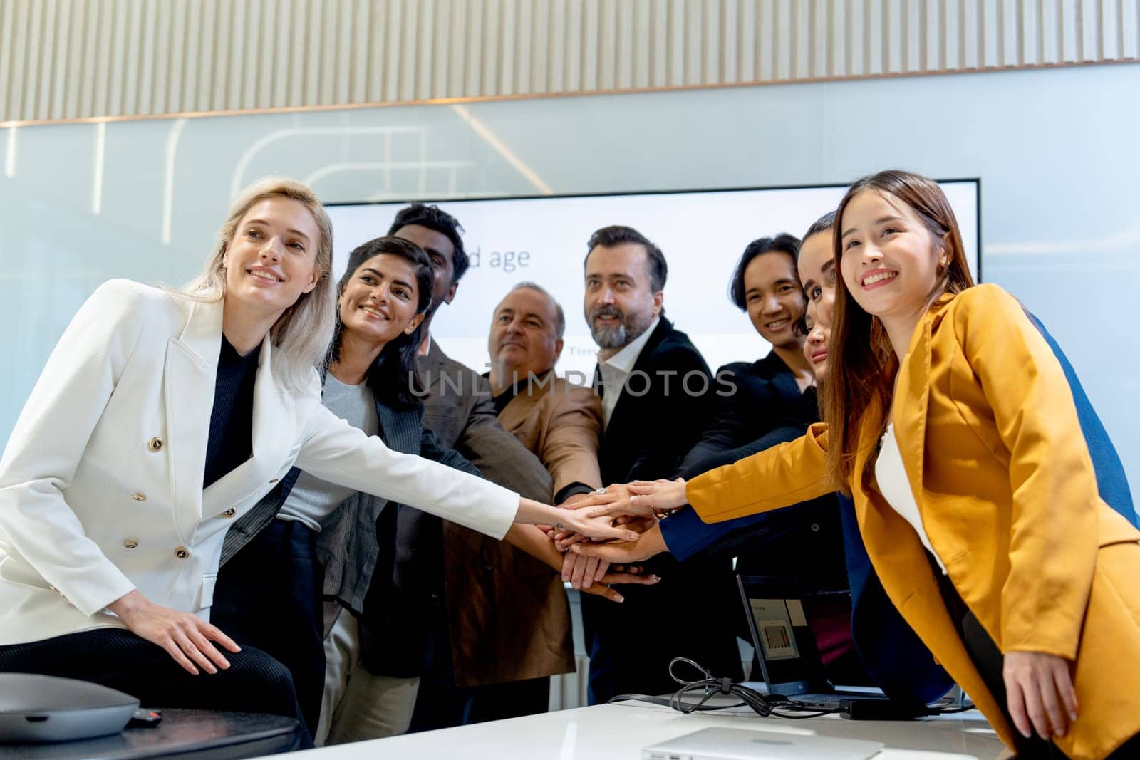 Group of business men and women join hands and look forward with smiling in coference or meeting room.