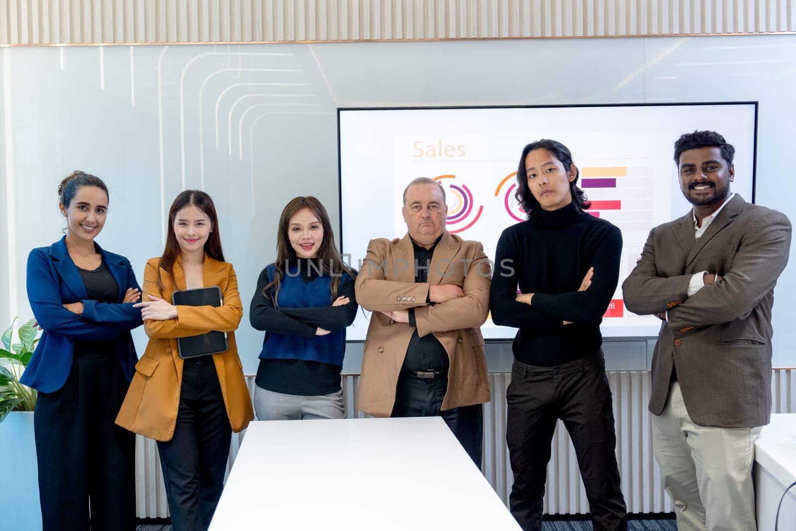 Portrait of multiethnic business men and women stand with arm crossed and look at camera in front of the monitor in conference room.