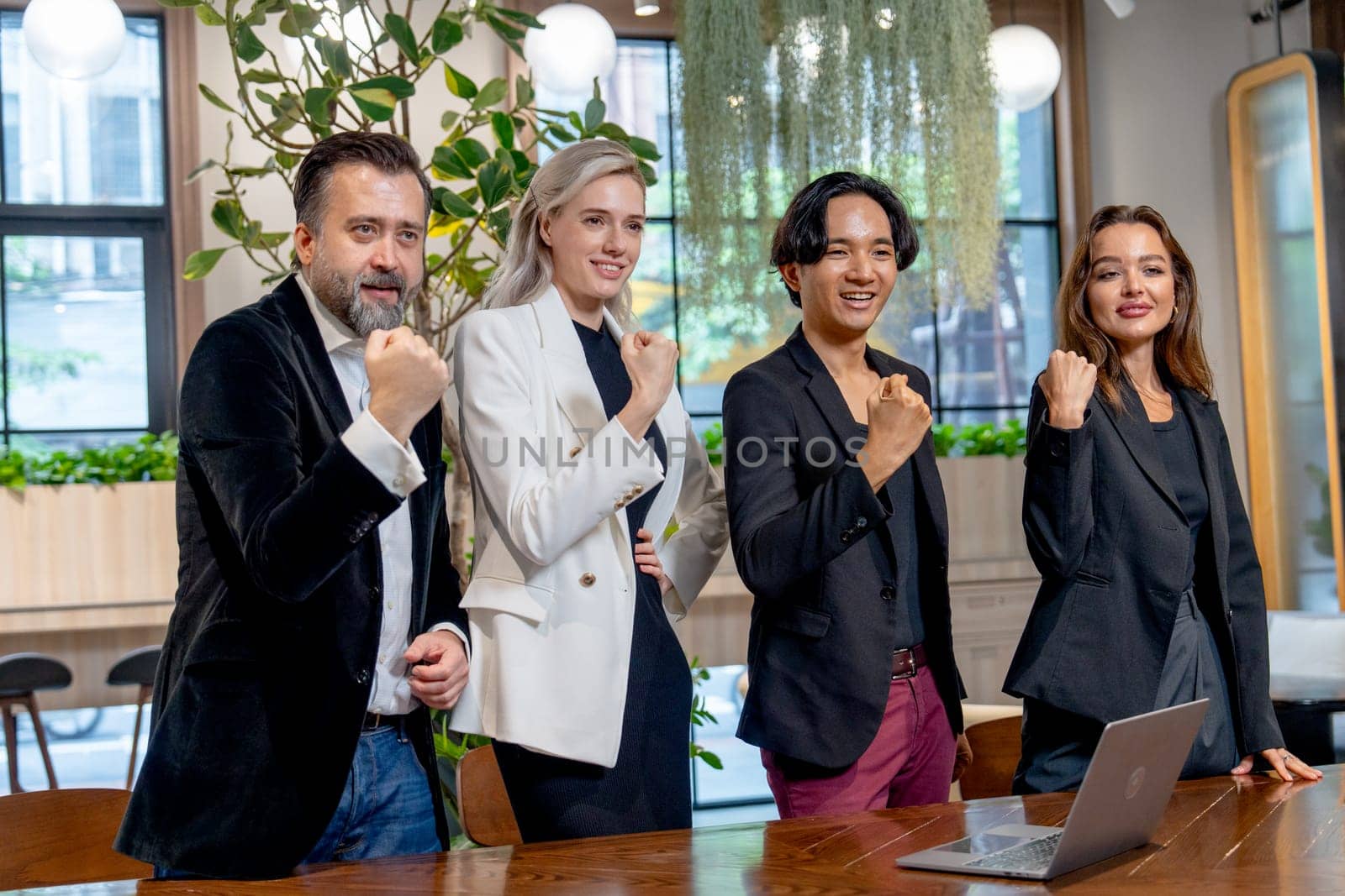 Portrait of Caucasian and Asian business men and women show fighting action and smile to their left side in area of coworking space in office.