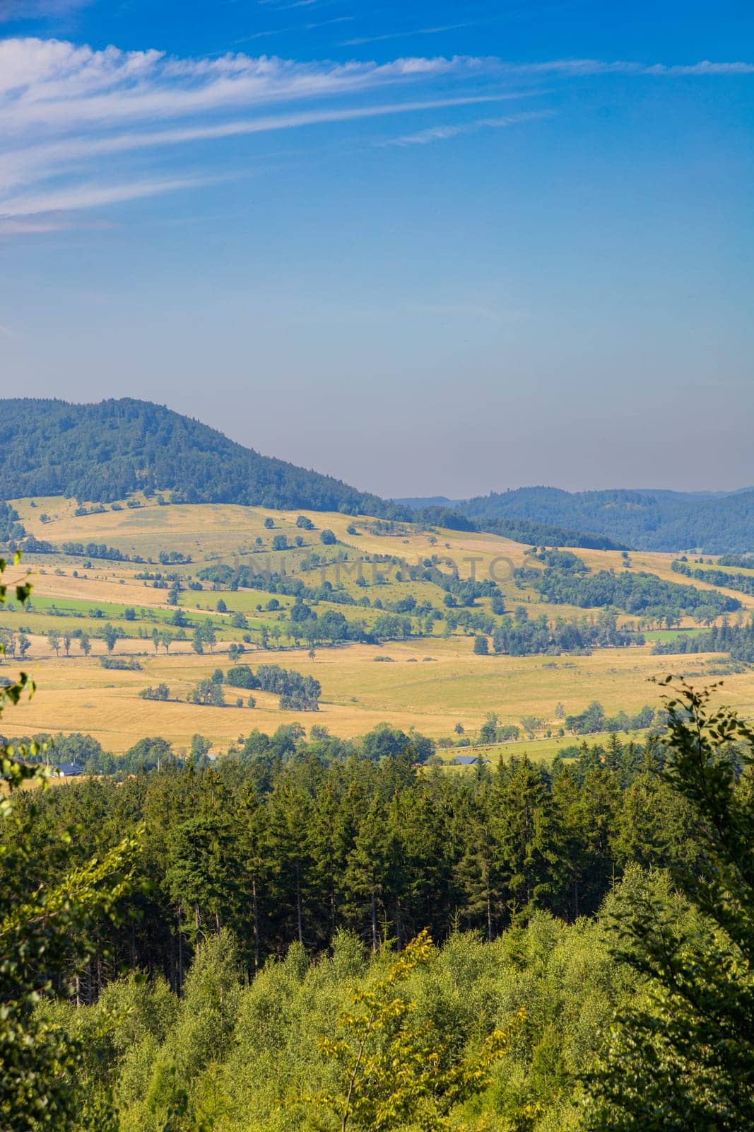 Beautiful green and blue panorama of layers of mountains and trees and some fields seen from top of viewing tower at highest mountain in this area