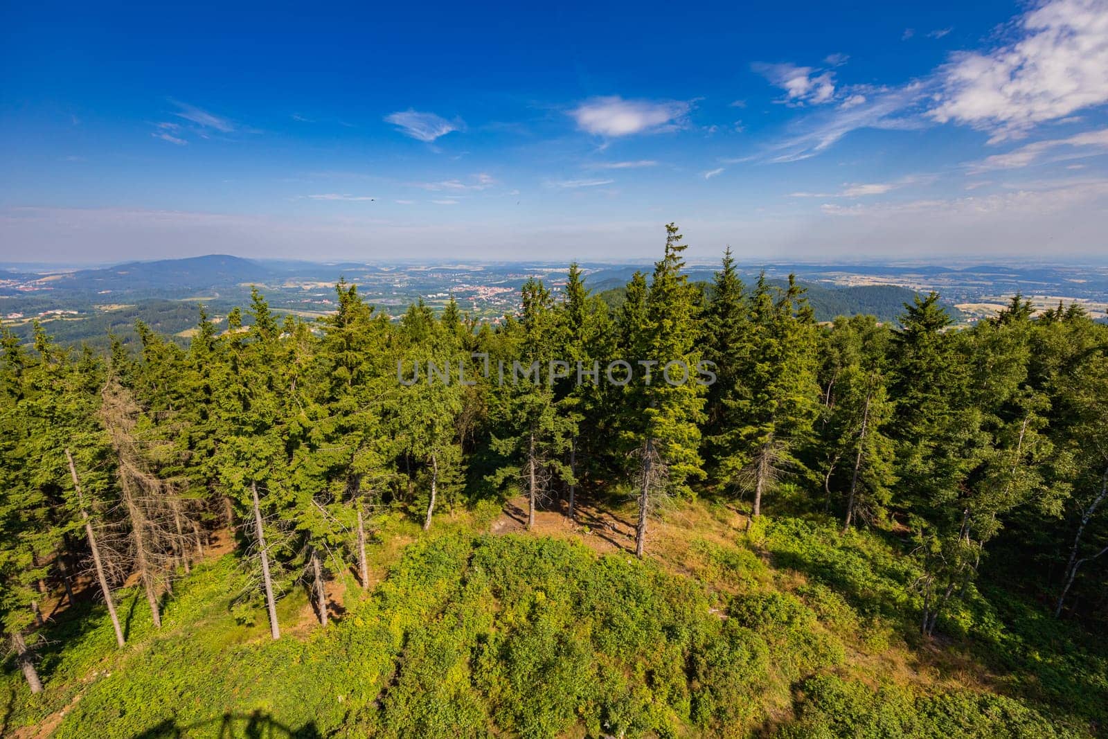 Beautiful green and blue panorama of layers of mountains and trees and some fields seen from top of viewing tower at highest mountain in this area