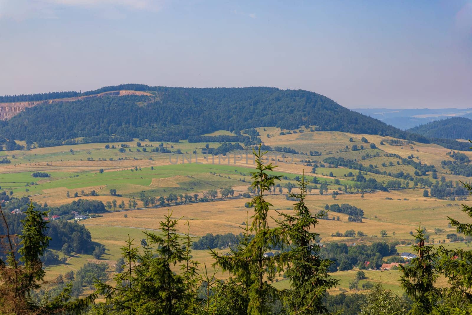 Beautiful green and blue panorama of layers of mountains and trees and some fields seen from top of viewing tower at highest mountain in this area