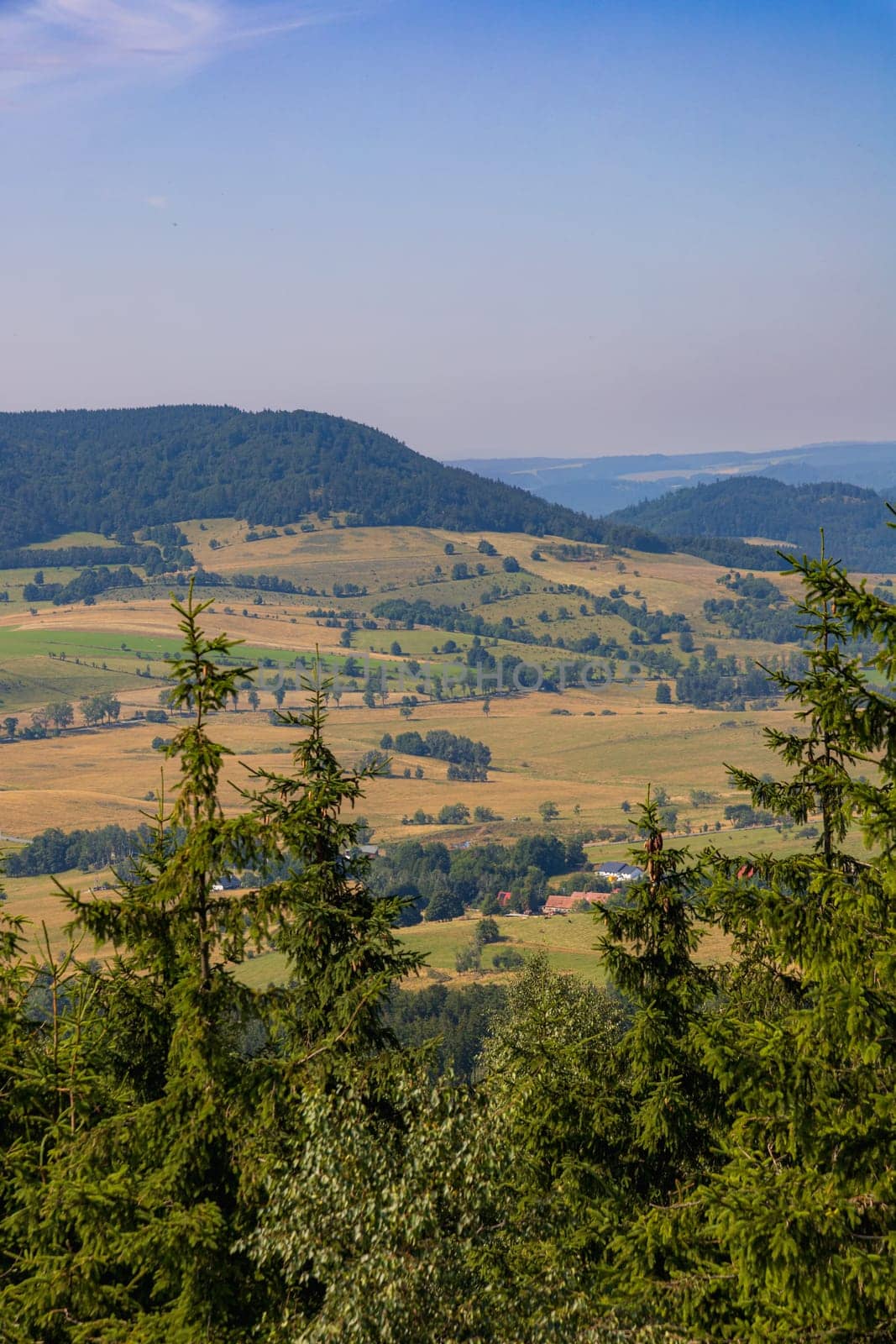 Beautiful green and blue panorama of layers of mountains and trees and some fields seen from top of viewing tower at highest mountain in this area by Wierzchu