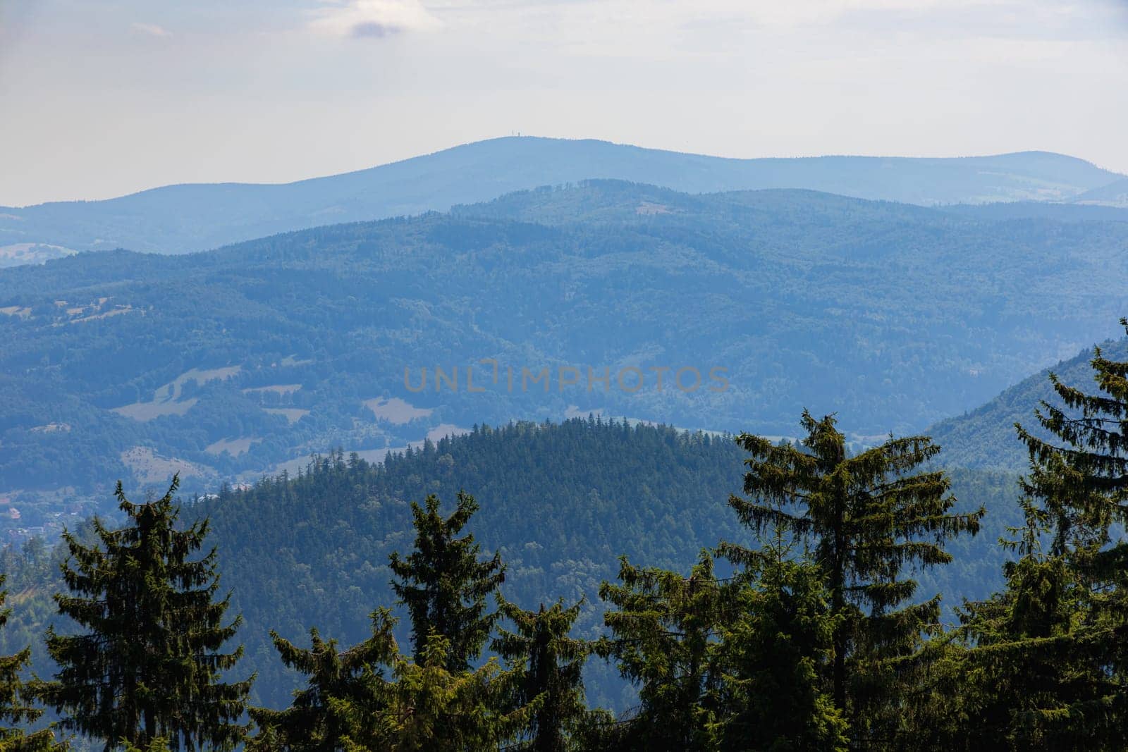 Beautiful green and blue panorama of layers of mountains and trees and some fields seen from top of viewing tower at highest mountain in this area