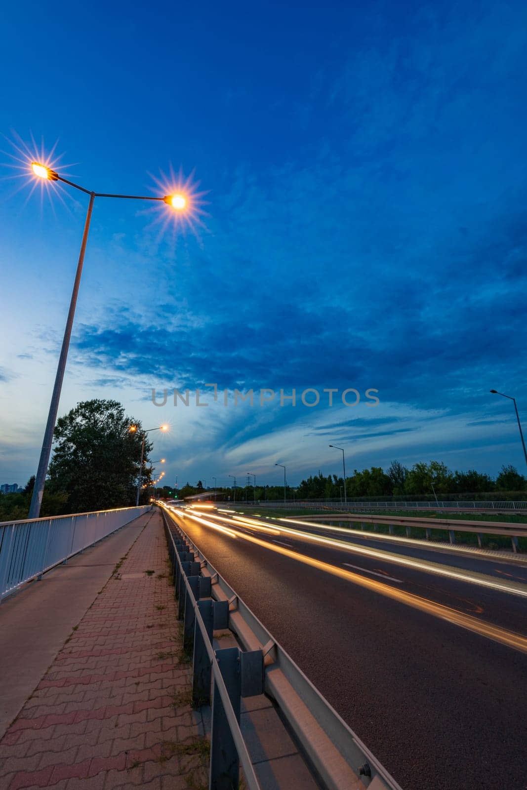 Long streaks of light made by riding cars on the road on the bridge at cloudy afternoon