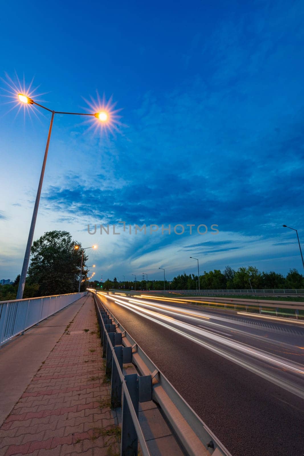 Long streaks of light made by riding cars on the road on the bridge at cloudy afternoon by Wierzchu