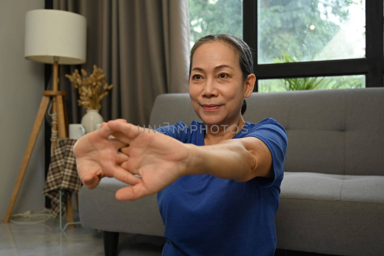 Happy retired woman in sportswear doing stretching exercises at home. Sports and Healthy lifestyle concept