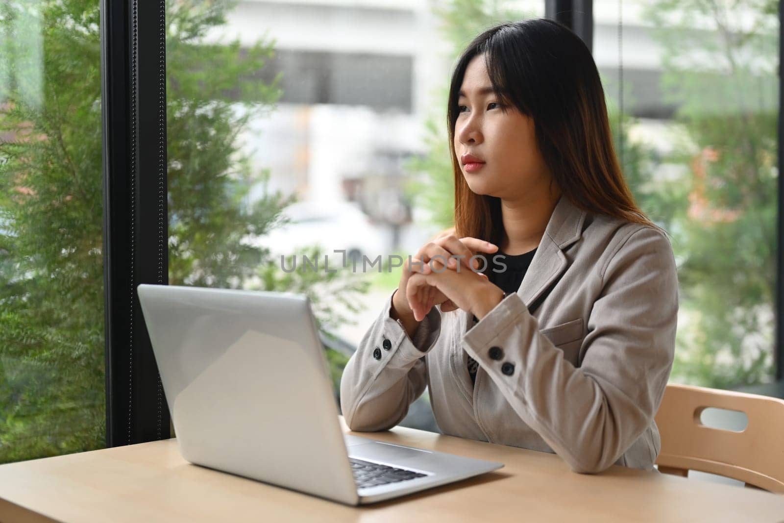 Thoughtful young woman sitting at workplace looking away dreaming of future or thinking on new ideas