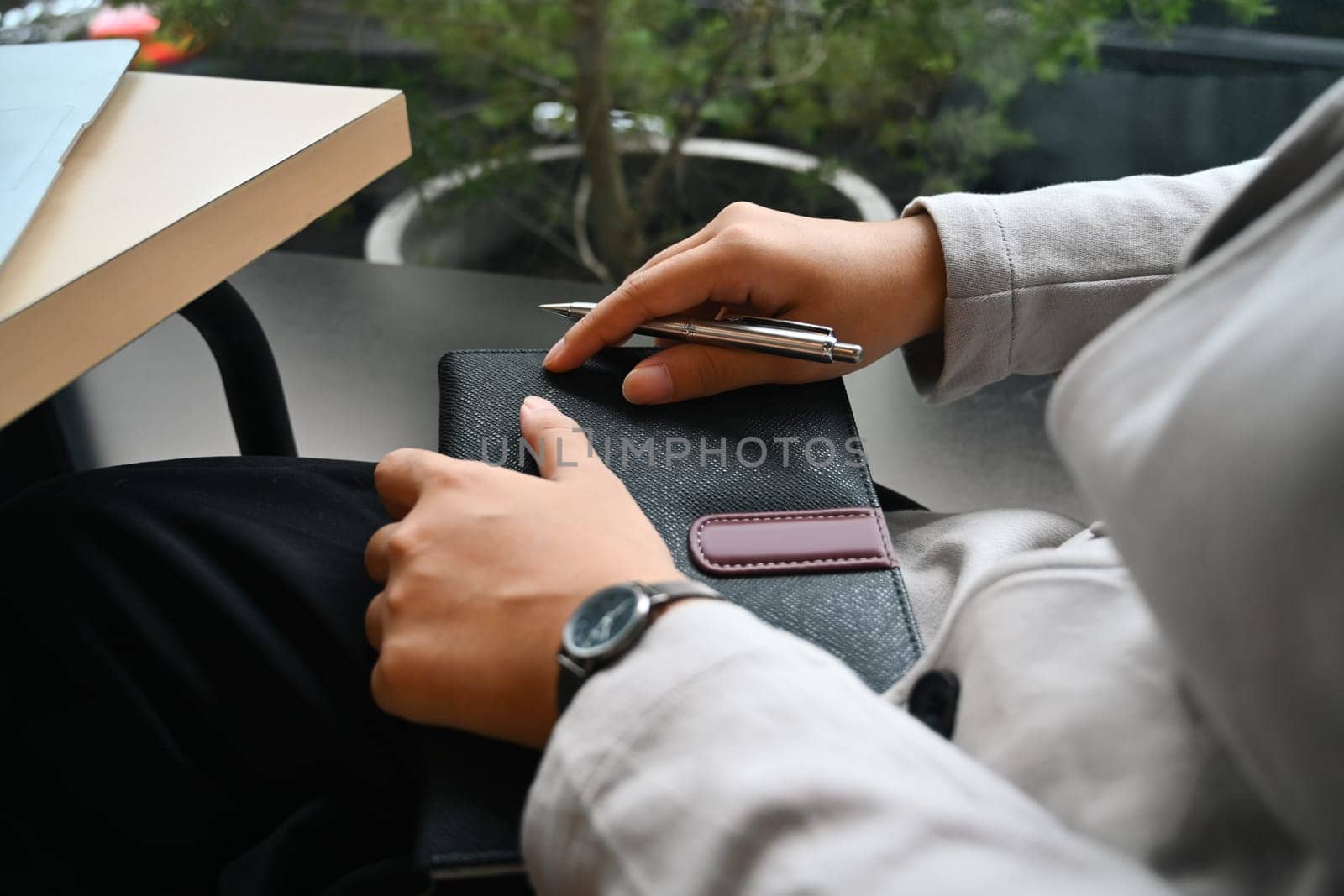 Cropped shot of businesswoman with leather journal notebook sitting near office window