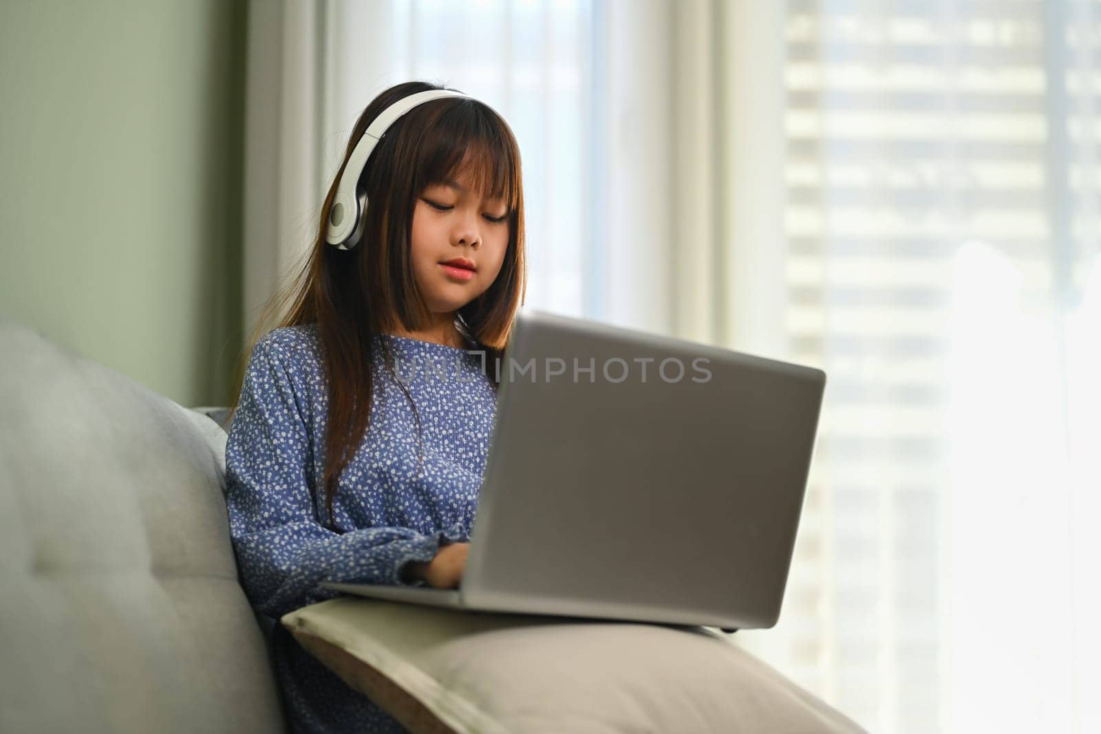 Cute schoolgirl in headphone watching online virtual class on laptop. Education concept. by prathanchorruangsak