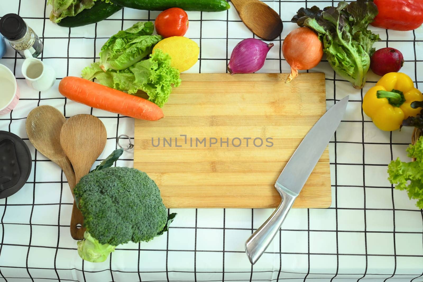 Top view knife and wooden cutting board surrounded by fresh vegetables on kitchen table. Healthy food concept. by prathanchorruangsak