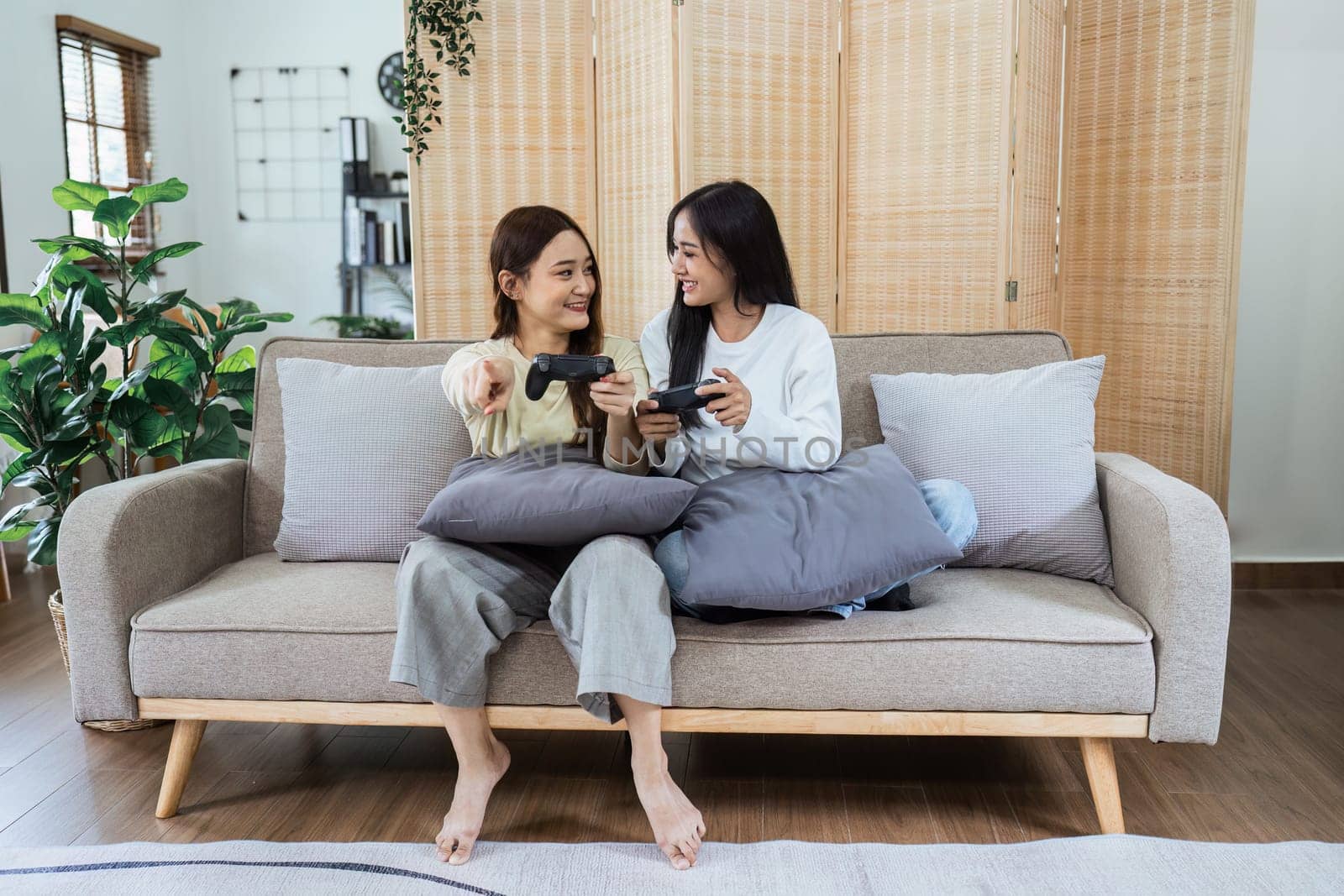 Young woman lesbian couple sitting on the comfortable sofa and playing game console while spending time together in living room at home by itchaznong