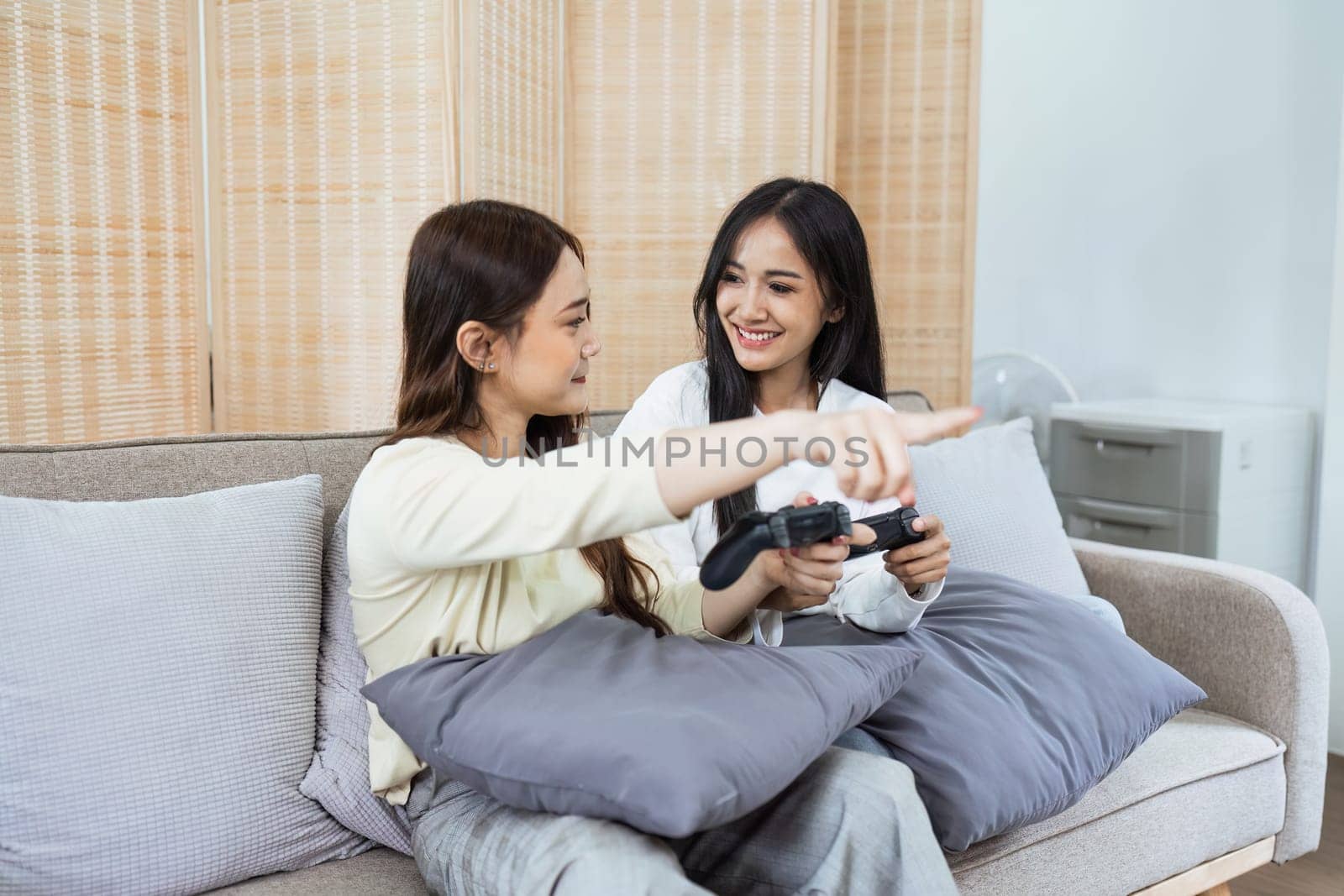 Young woman lesbian couple sitting on the comfortable sofa and playing game console while spending time together in living room at home by itchaznong