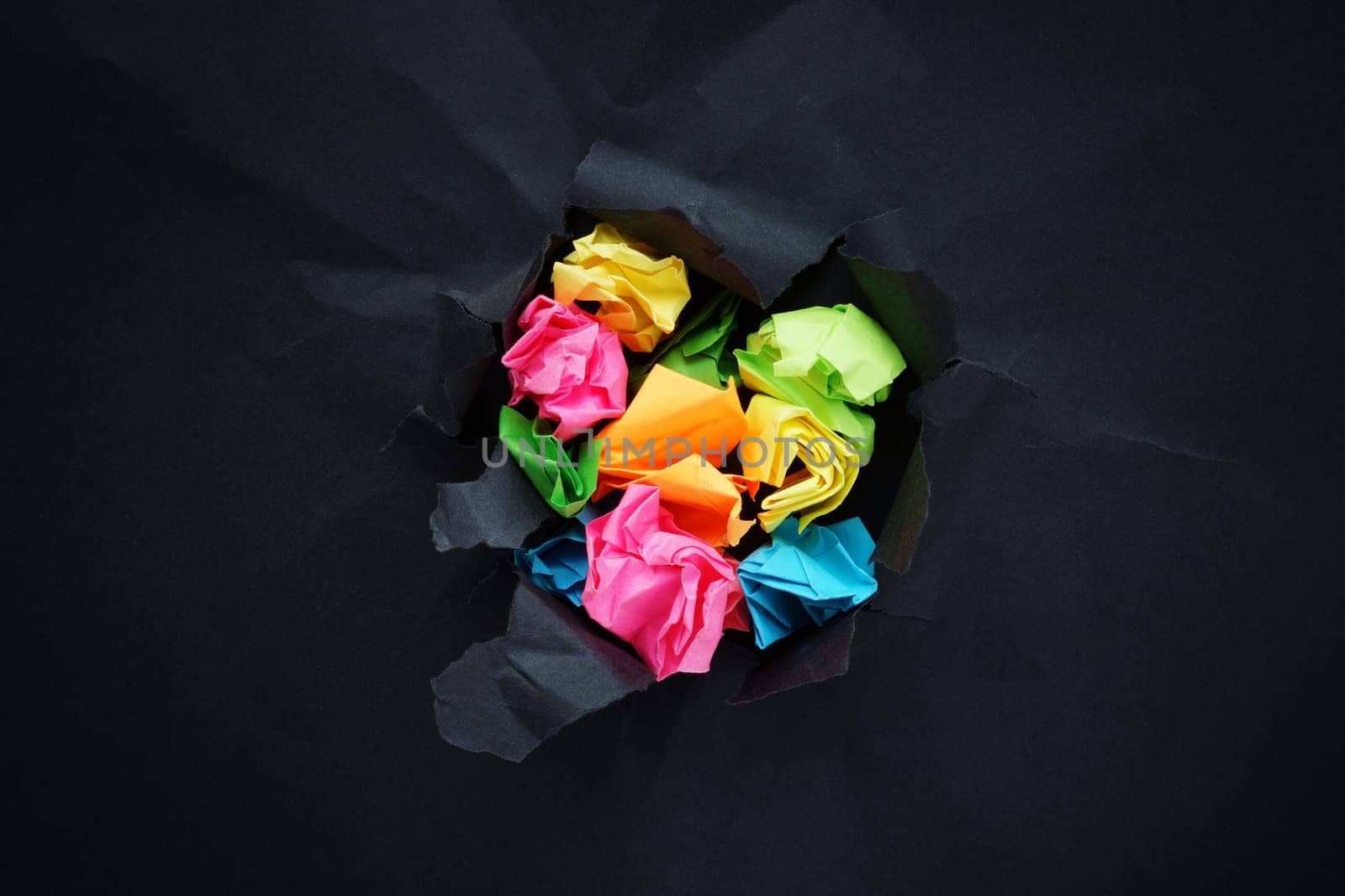 Abstract concept of positivity and treatment of depression. Multicolored paper balls break through black paper.