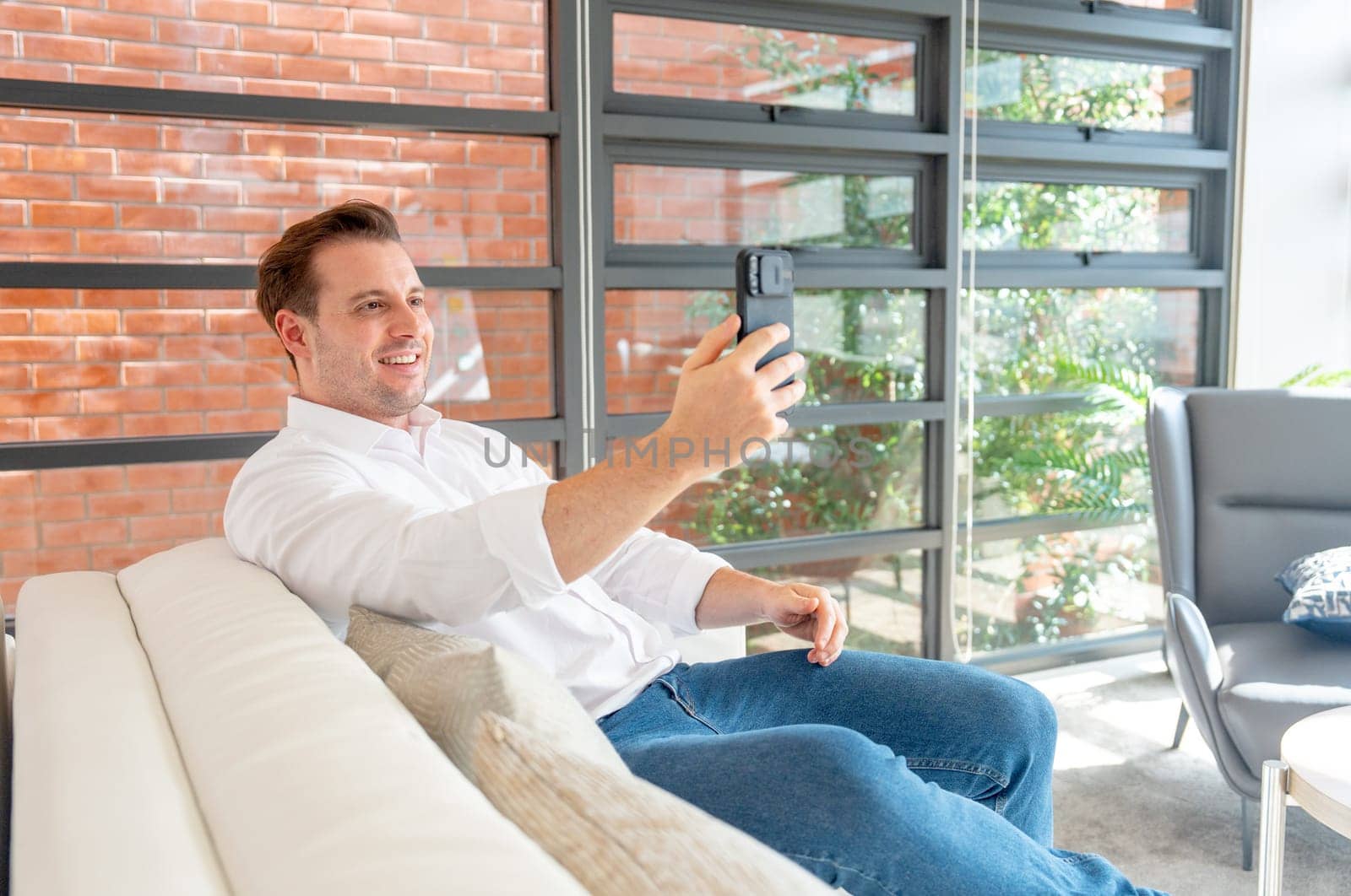 Portrait of smart Caucasiness business man lie or sitting on sofa and use mobile phone to facetime or online meeting with other with day light.